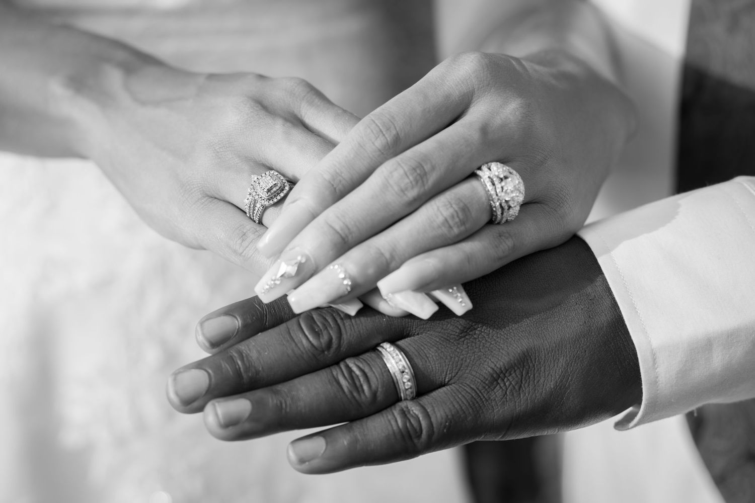 Black and white close-up of bride and groom's hands showing wedding rings with decorative nails.