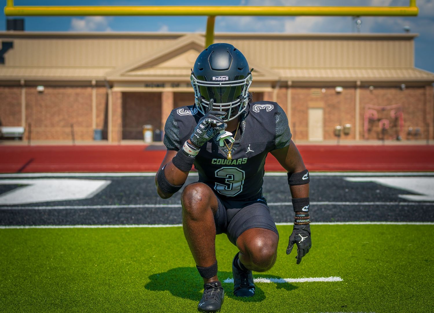 Football player in teal uniform number 3 crouching in ready stance on field.