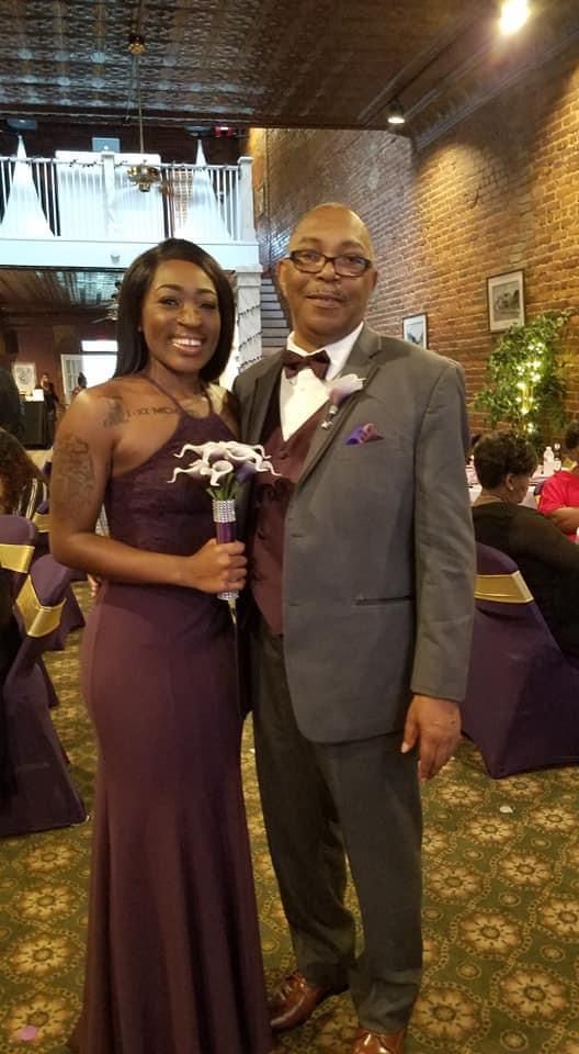 Man and woman dressed in purple formal attire posing together at an elegant banquet event.