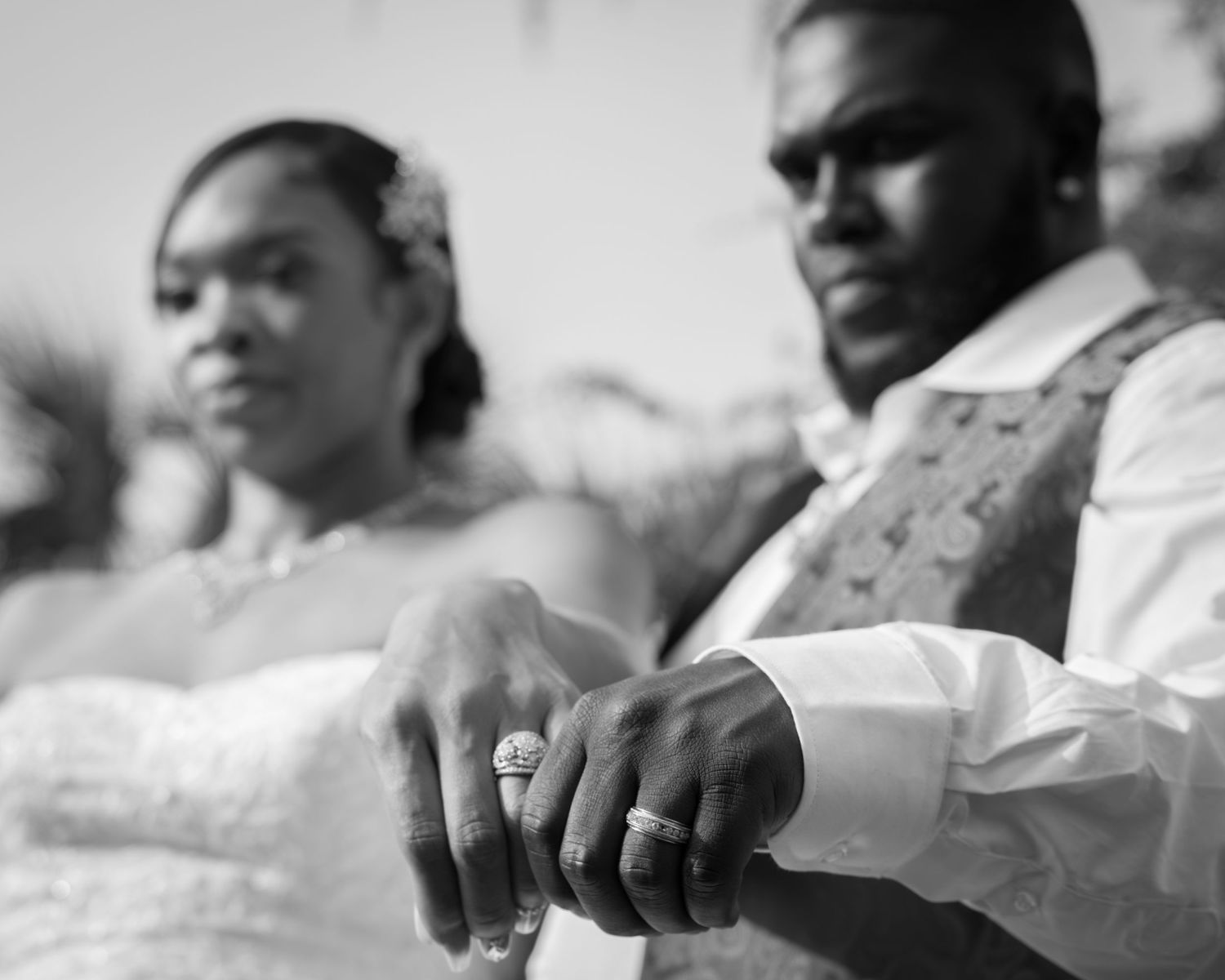 Black and white photo of newlyweds displaying wedding rings at outdoor ceremony.
