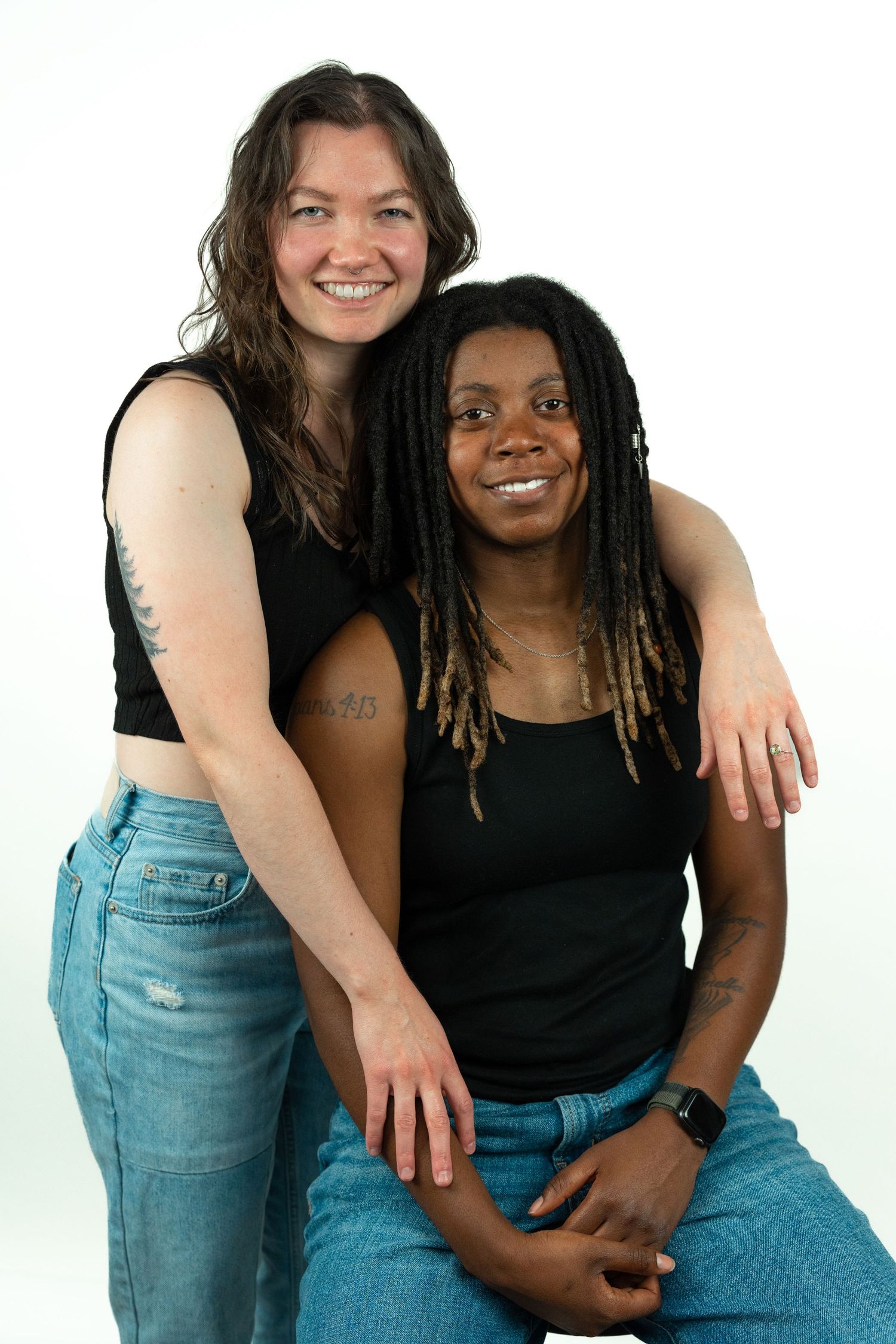 Two smiling women posing together in matching black tops and jeans in a white studio setting.