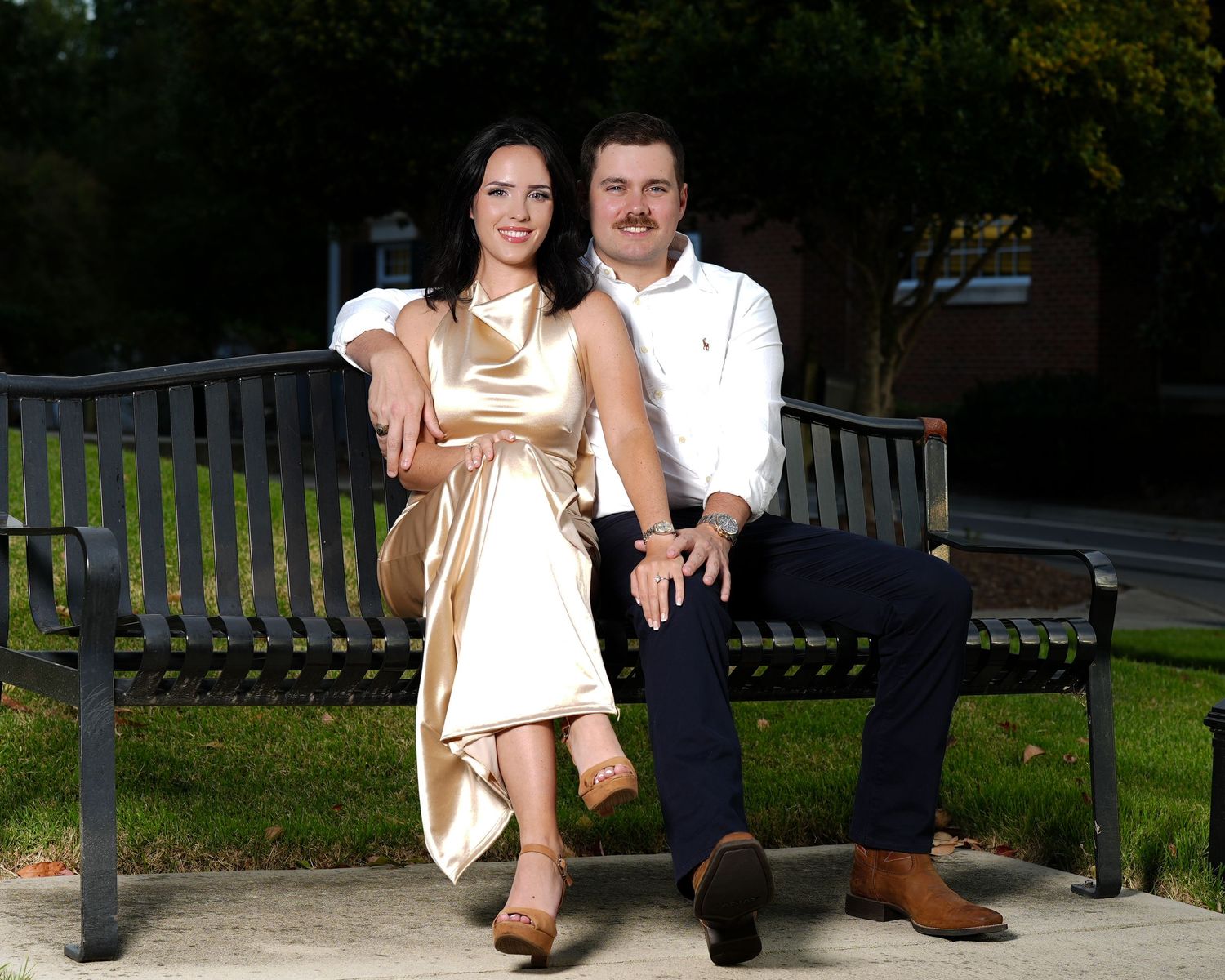 Couple sitting together on a park bench smiling outdoors in casual elegant attire.