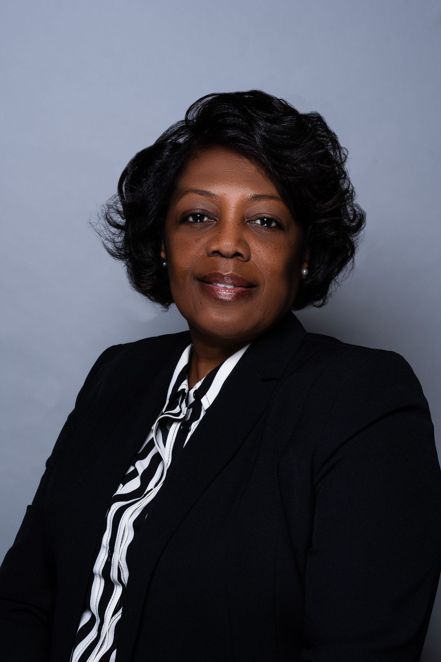 Professional Black woman in black blazer and striped blouse smiling for portrait photo.