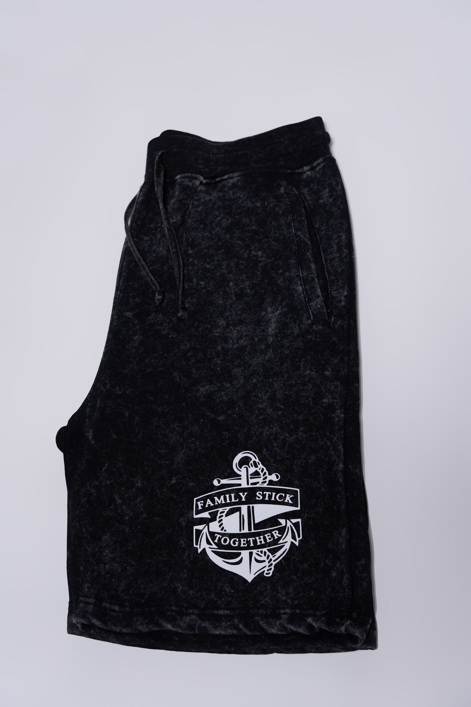 Black acid wash drawstring shorts with white Family Stick Together anchor logo graphic.