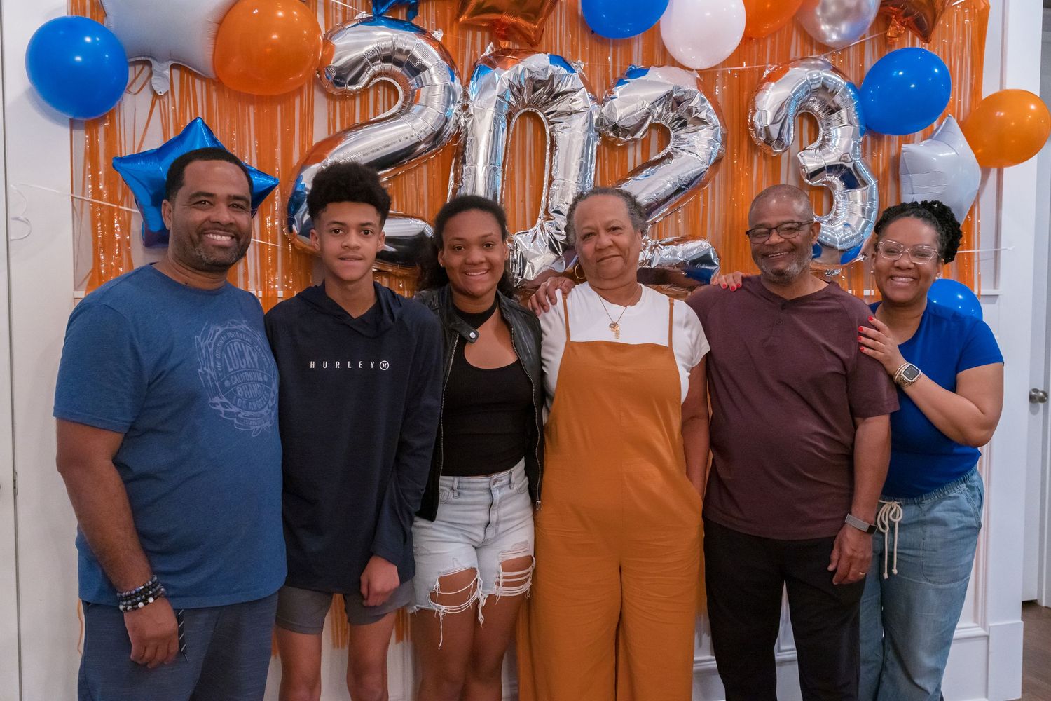 Family of six smiling together in front of silver 2023 balloons at a graduation celebration.