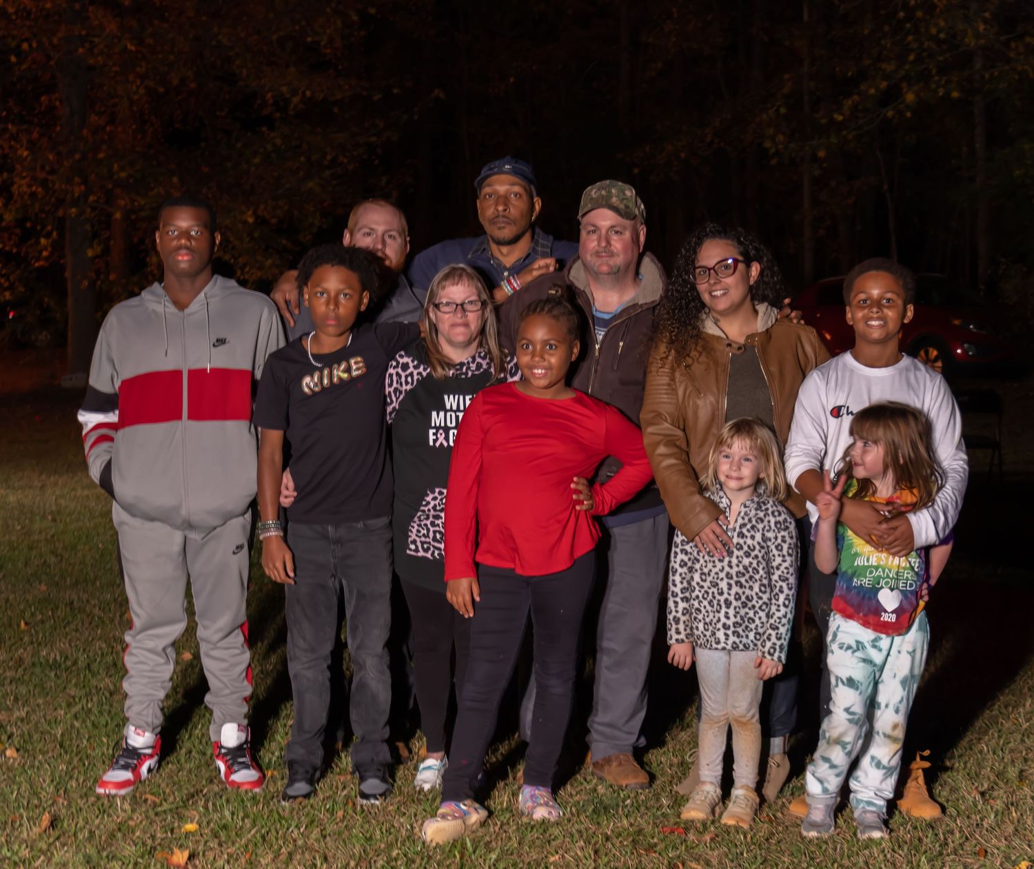 Large multigenerational family group posing together outdoors at night on a grassy lawn.