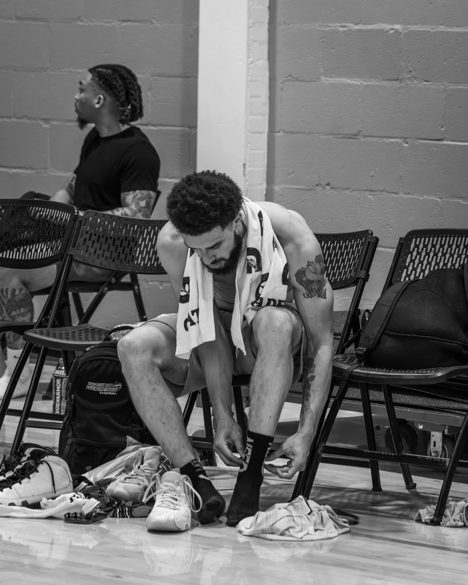 Black and white photo of basketball player tying shoes on sideline bench before game.