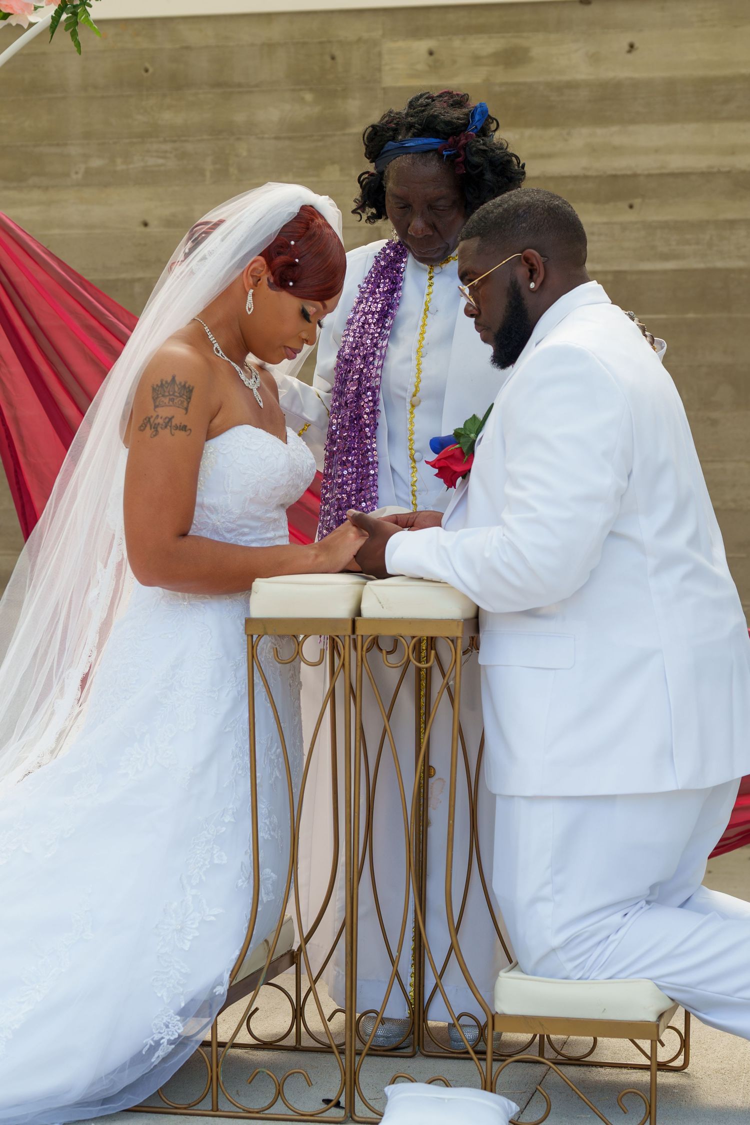 Bride and groom kneeling in prayer together at wedding altar with officiant during ceremony.
