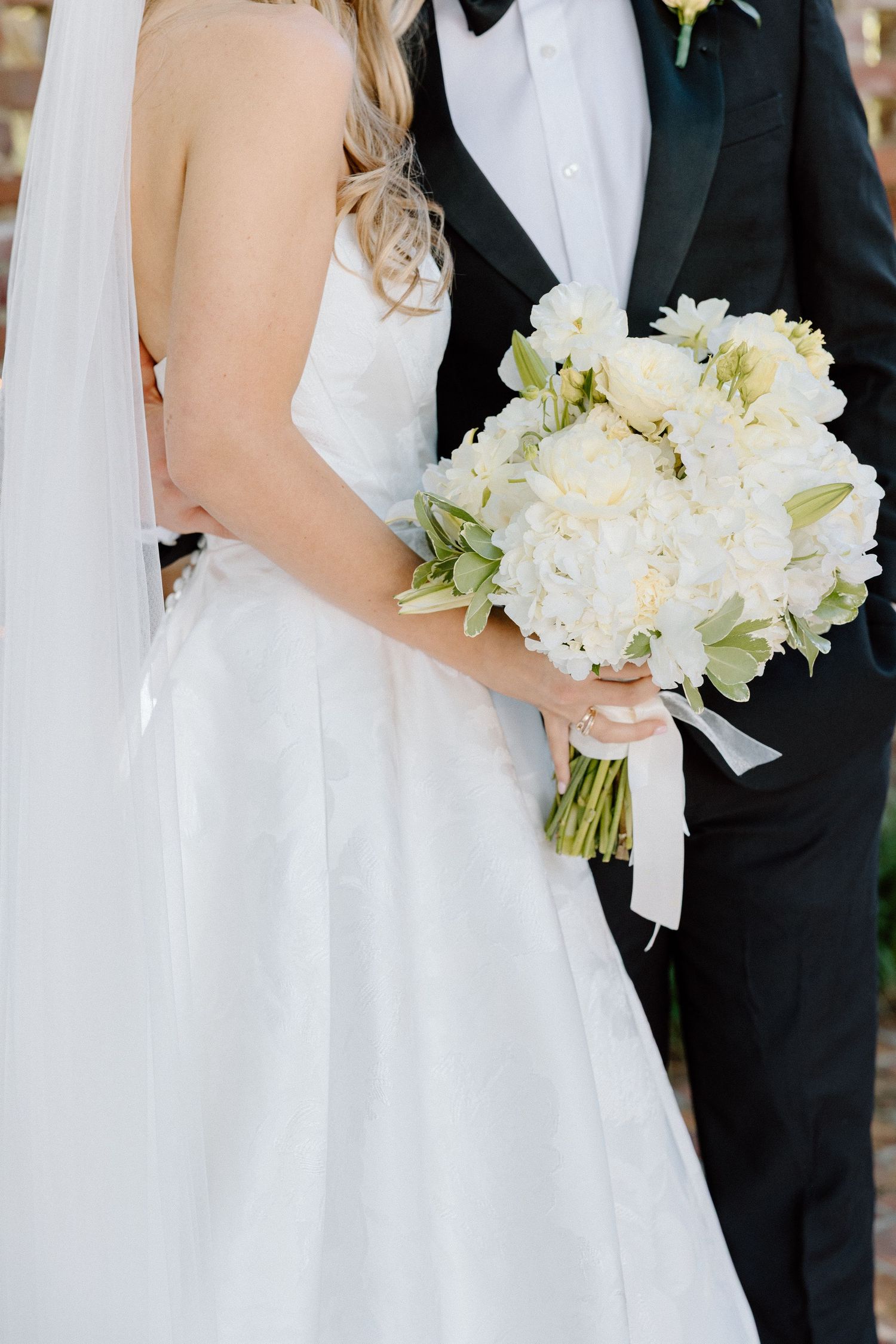 Bride and groom holding a white floral bouquet with ribbon at their wedding ceremony.