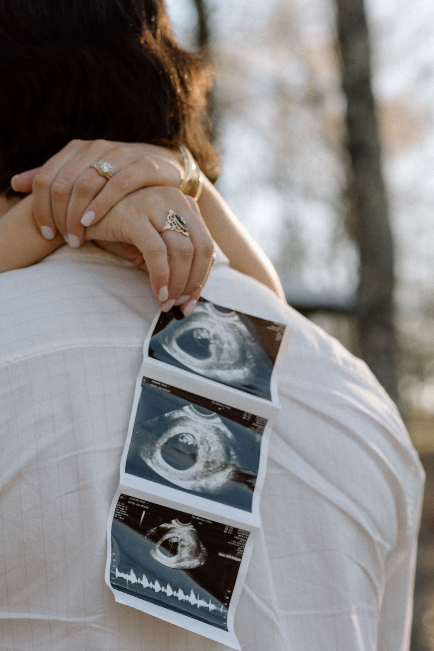 Close-up of couple embracing with ultrasound photos held against a white shirt during pregnancy announcement session.