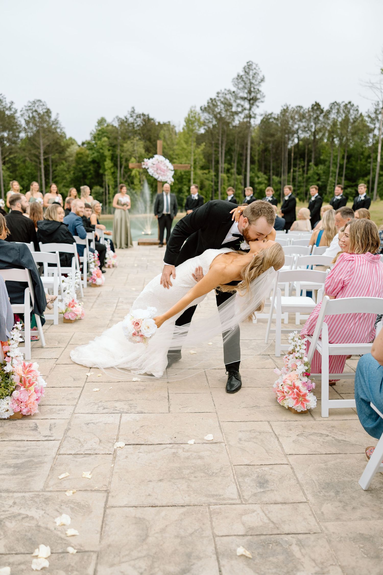 Groom dips bride for a romantic kiss during outdoor wedding ceremony recessional on stone patio.