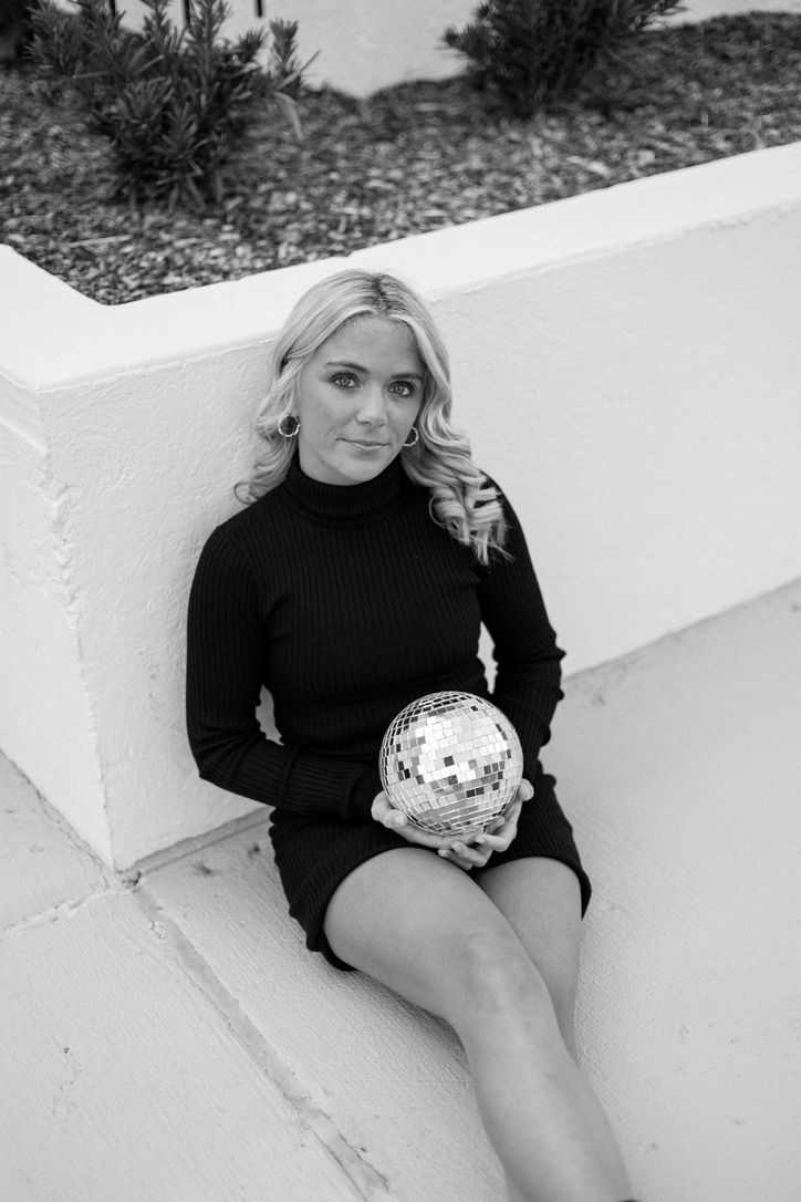 Blonde woman in black turtleneck dress holding disco ball in black and white portrait.