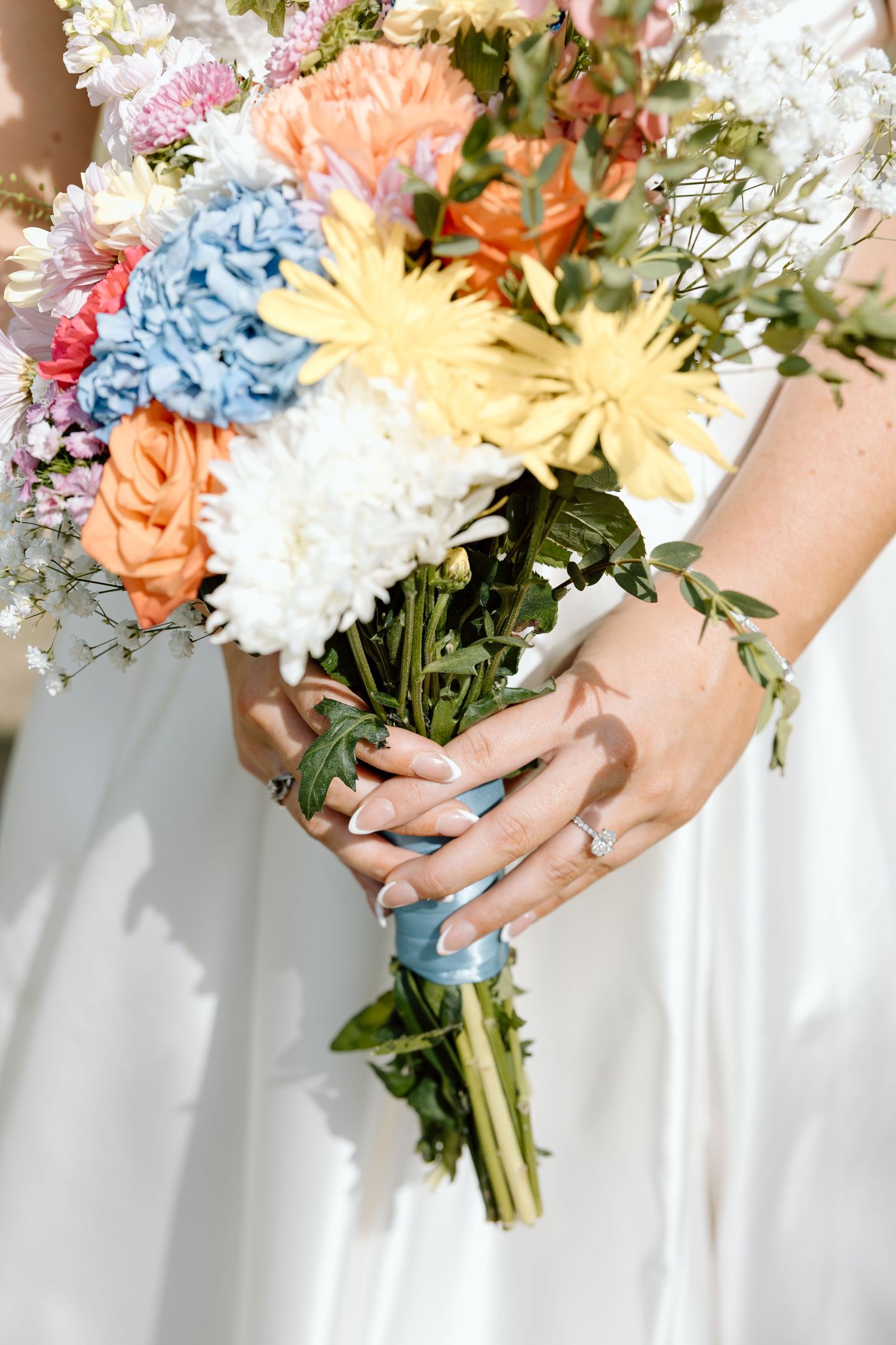 Bride holding colorful wedding bouquet with orange, blue, and yellow flowers.