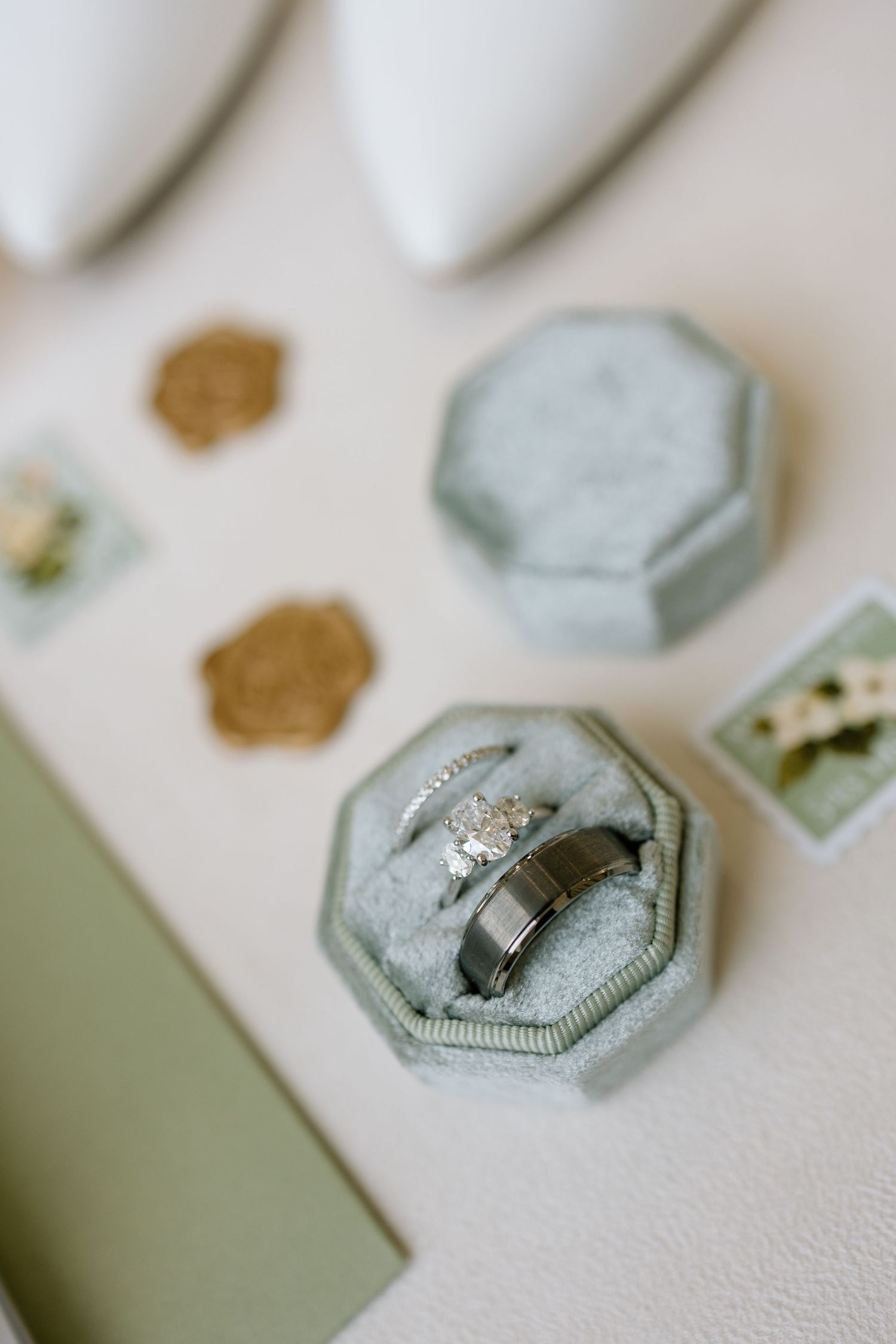 Wedding rings displayed in a sage green velvet ring box with gold wax seals nearby.