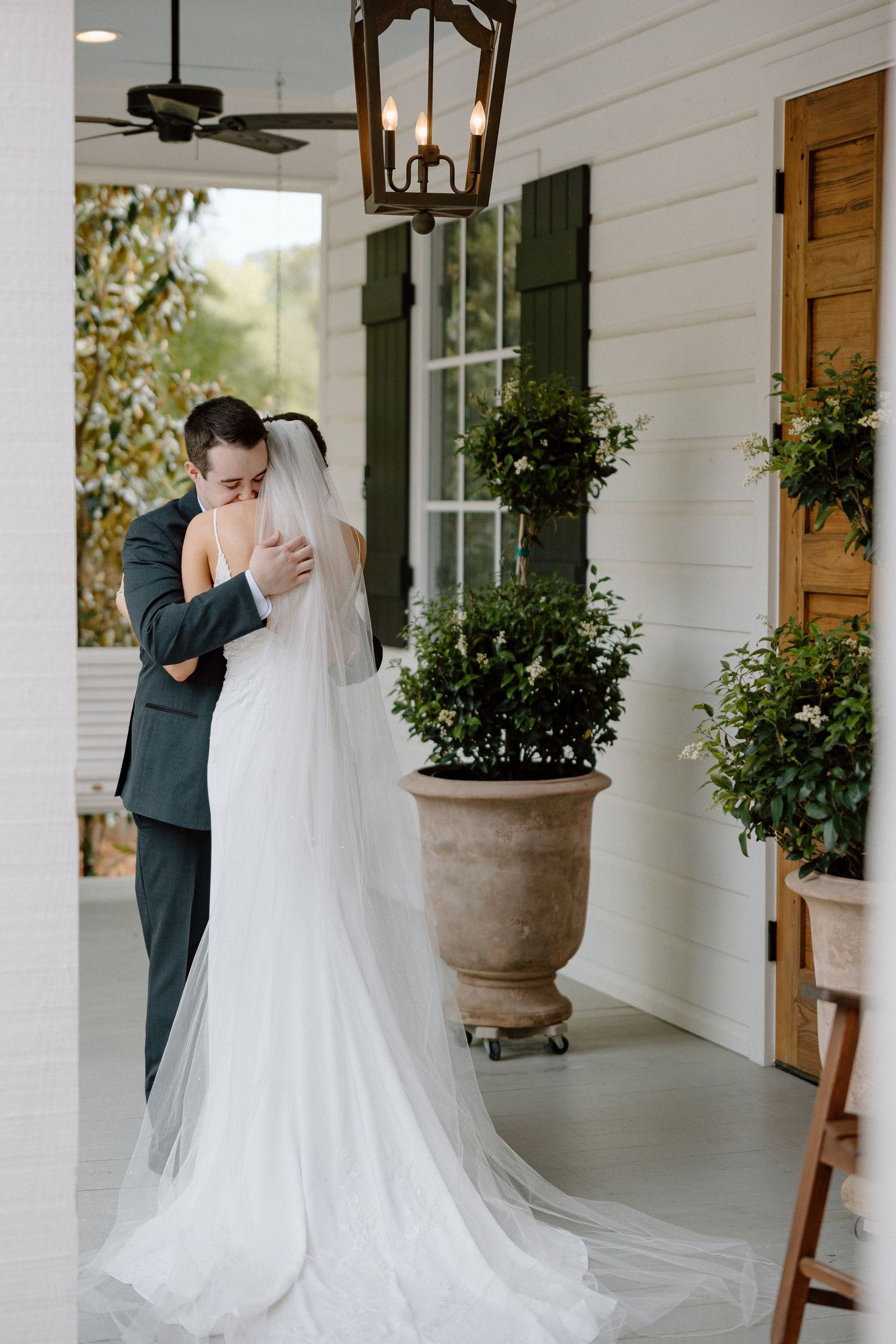 Bride and groom sharing first look embrace on a charming white Southern-style porch.