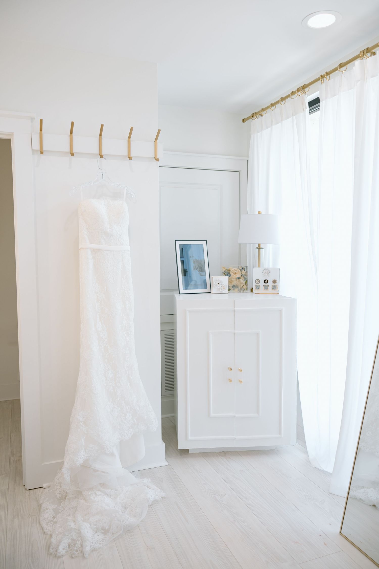 White lace wedding dress hanging in a bright, elegant white bridal suite room.