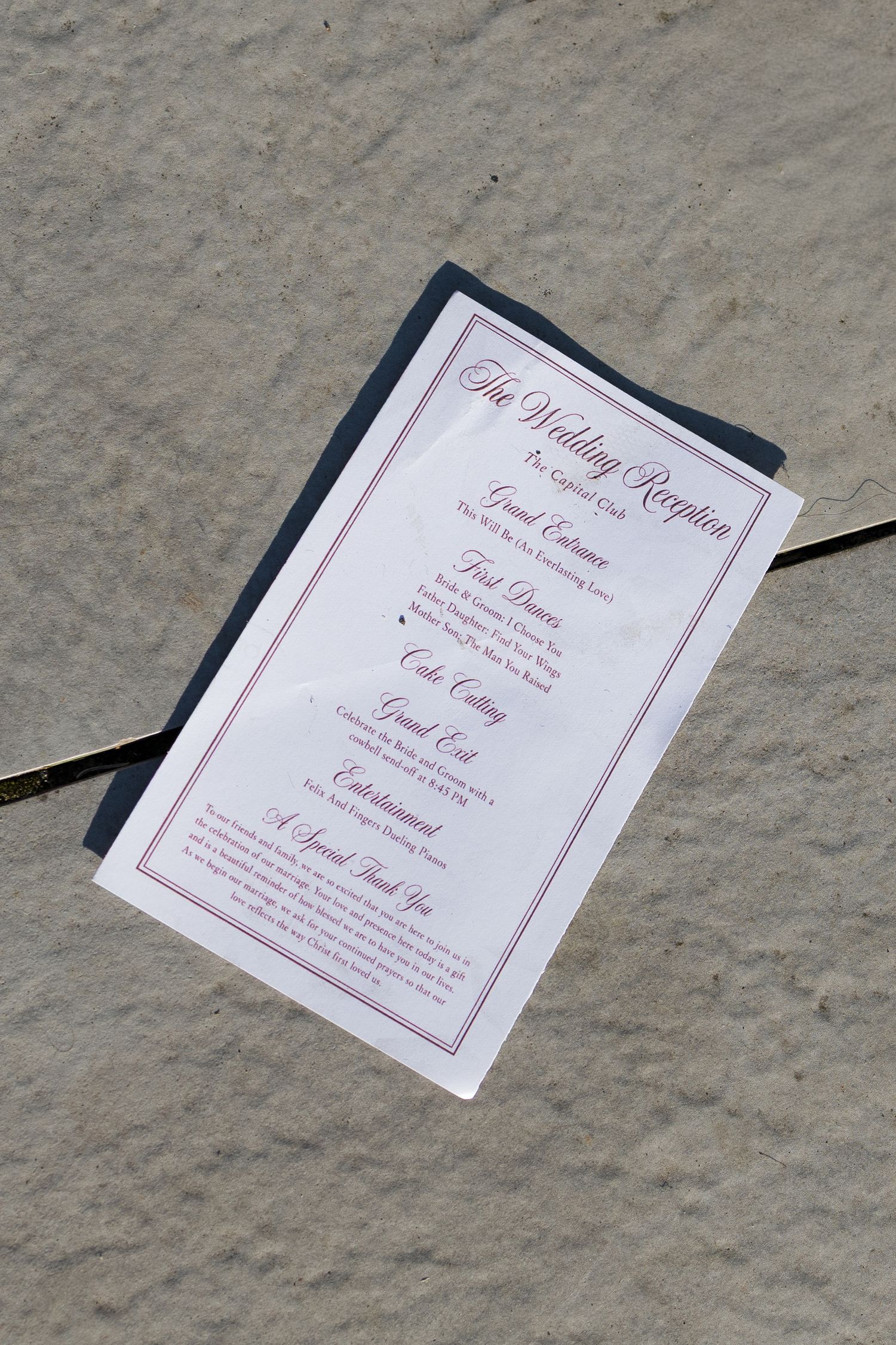 A wedding reception program card with elegant red script text resting on a stone surface.