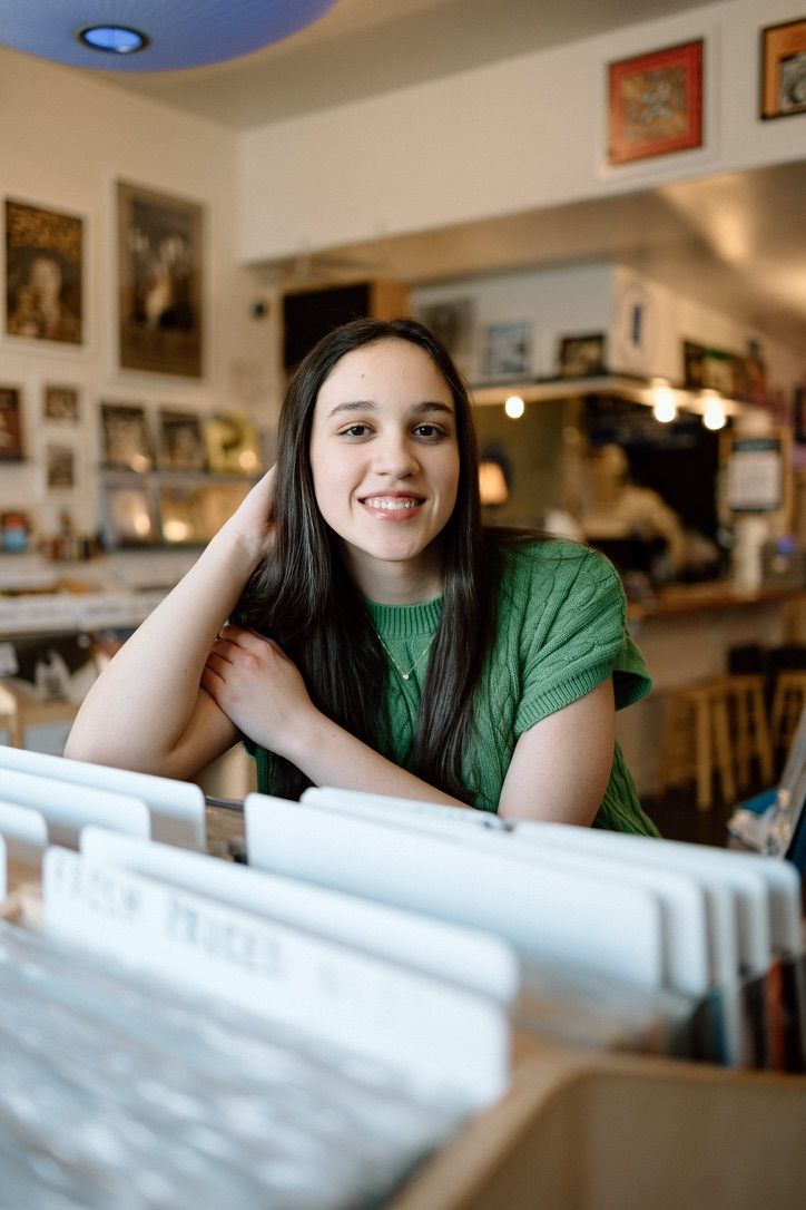 Smiling brunette teen girl posing among vinyl records in a music shop.