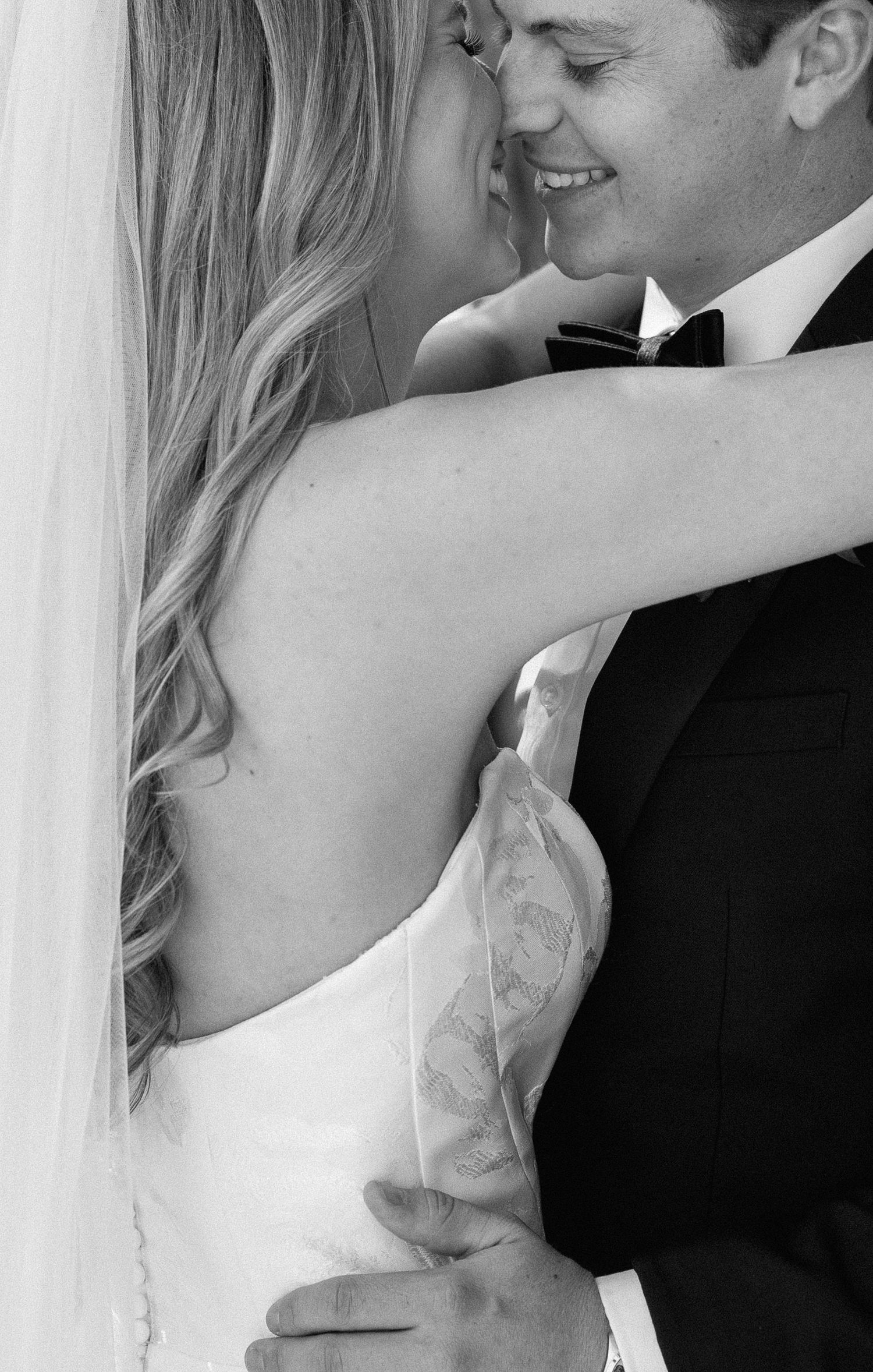 Black and white photo of smiling groom embracing bride in strapless wedding dress.