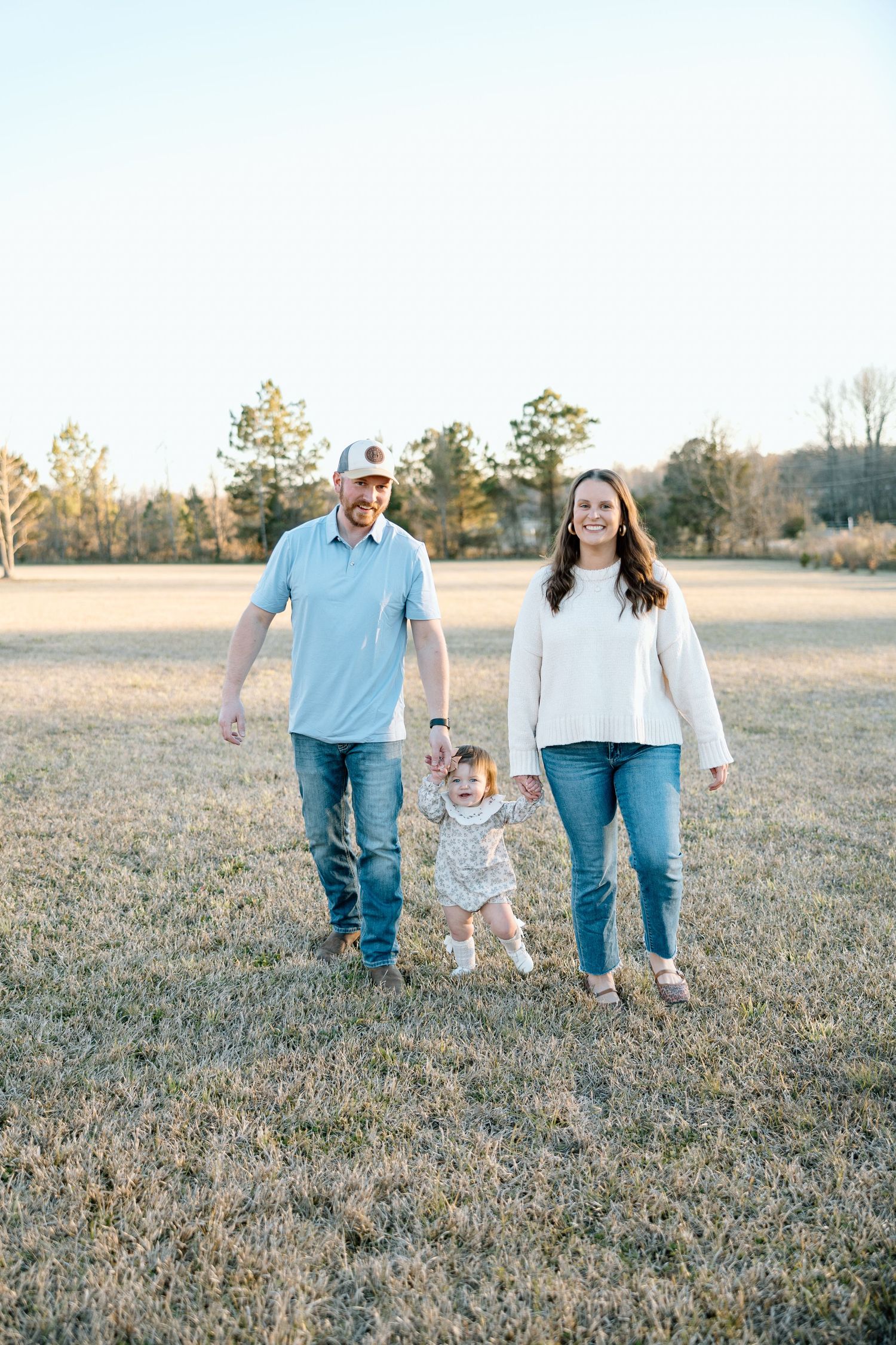 Happy young family with toddler walking together in an open field during golden hour sunset.