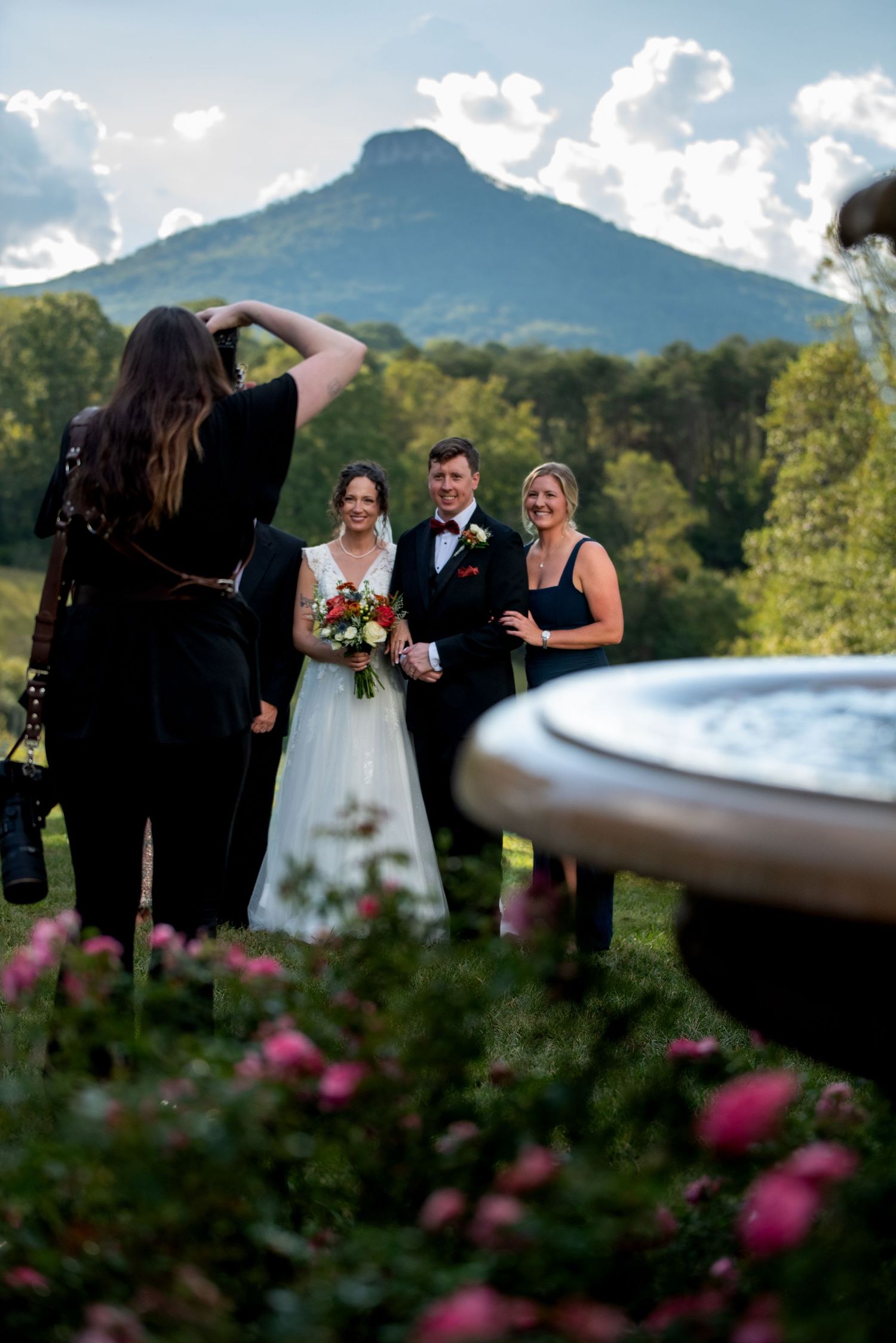 Wedding ceremony taking place outdoors with mountain views and pink flowers in the foreground.