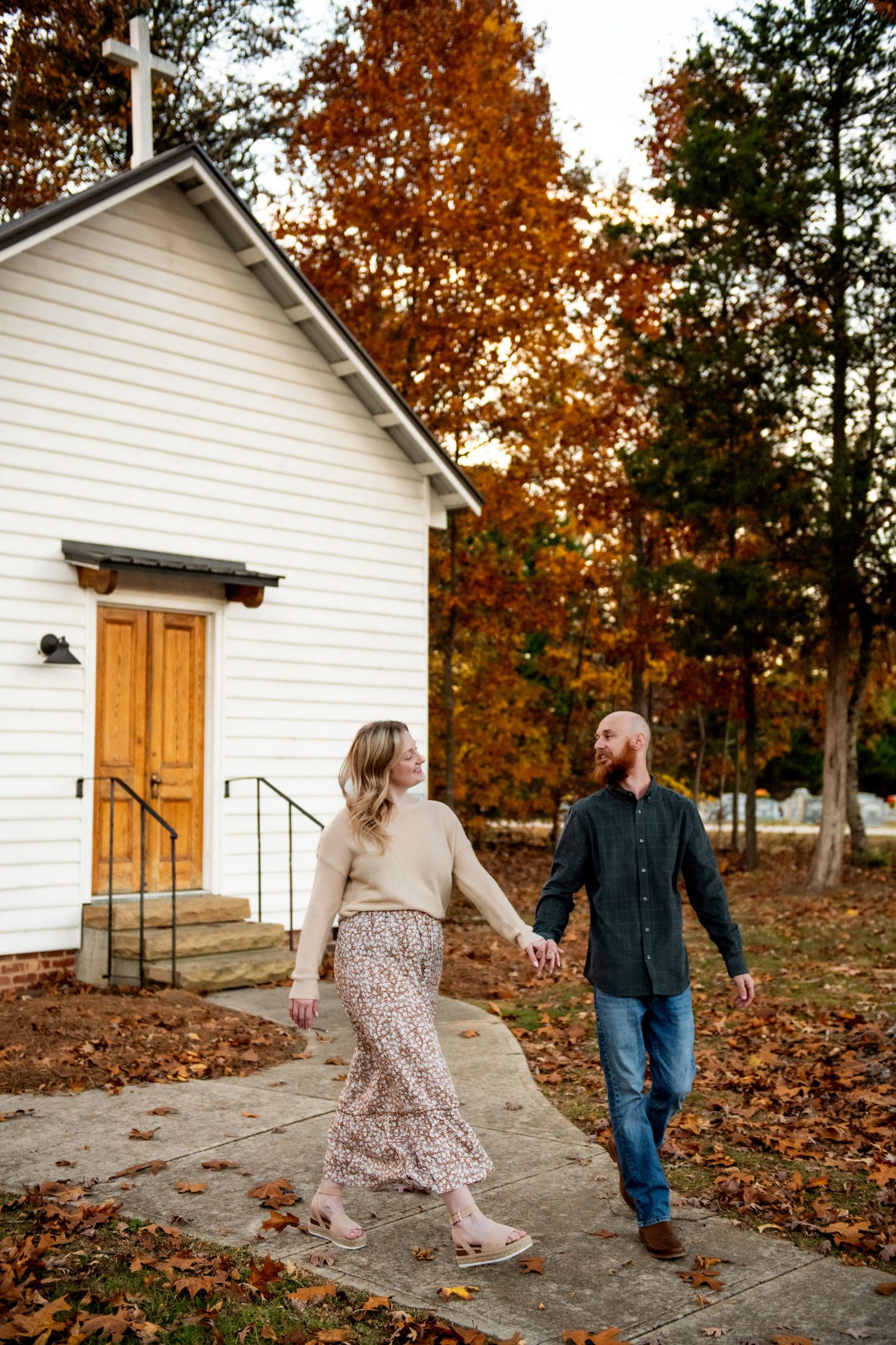 Couple playfully walking and dancing around a white country house surrounded by autumn foliage.
