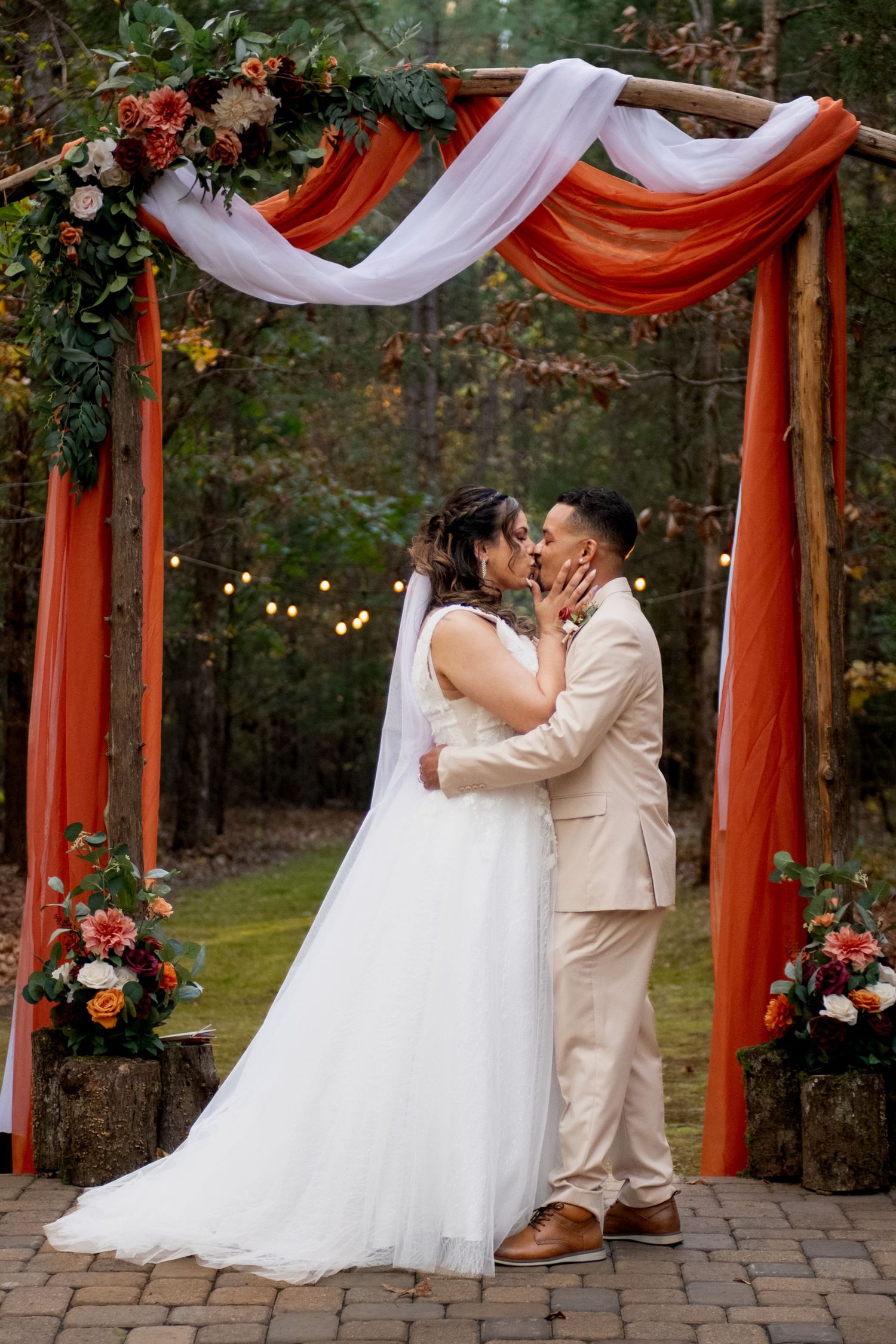 Wedding ceremony setup with red and white draped fabric arch decorated with flowers in an outdoor garden setting.
