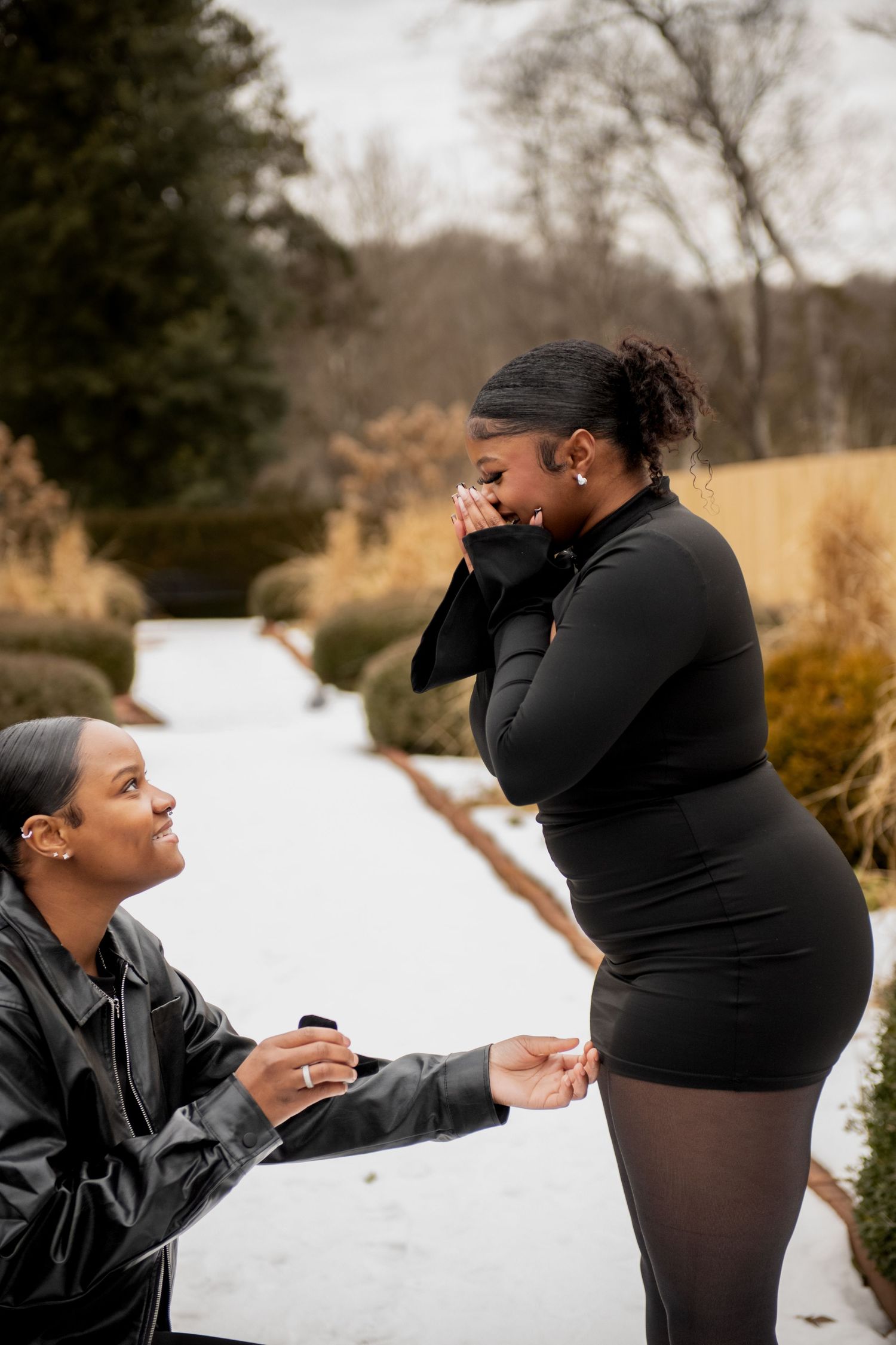 A romantic winter proposal moment on a snowy path with one person kneeling and presenting a ring.