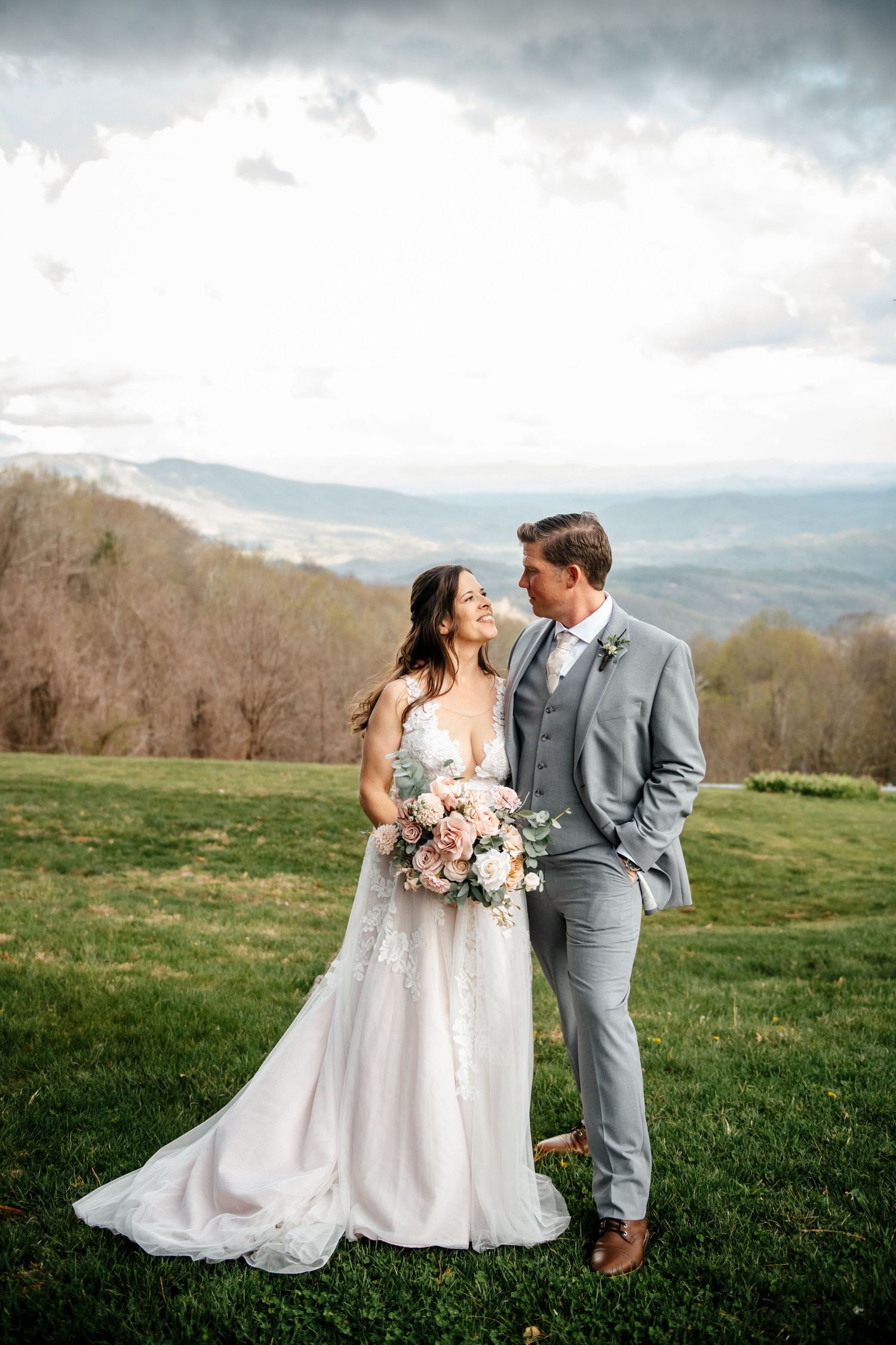 A bride and groom share a romantic moment on a green hillside with stunning mountain views on their wedding day.
