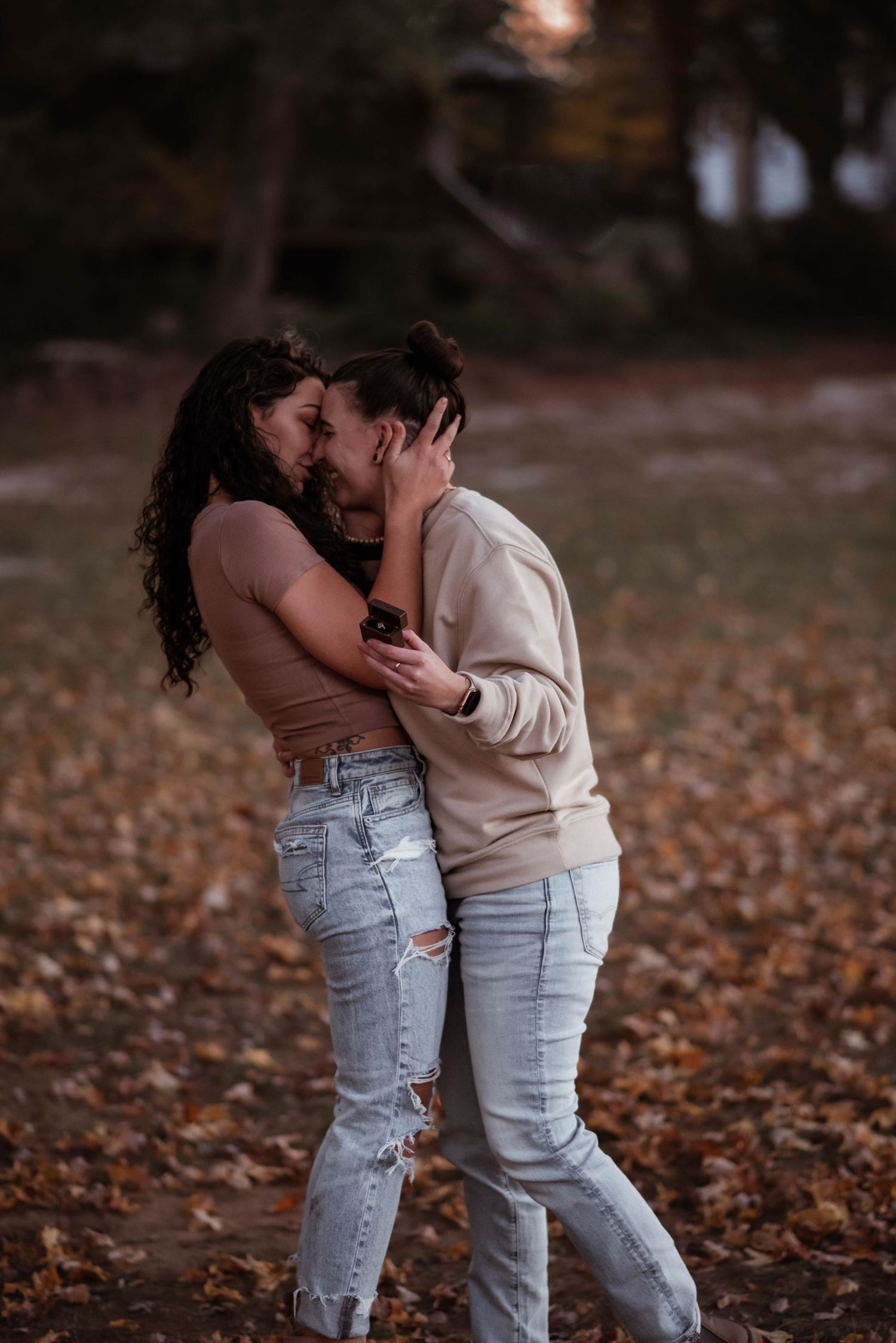 A couple shares an intimate moment while standing in autumn leaves on the ground.