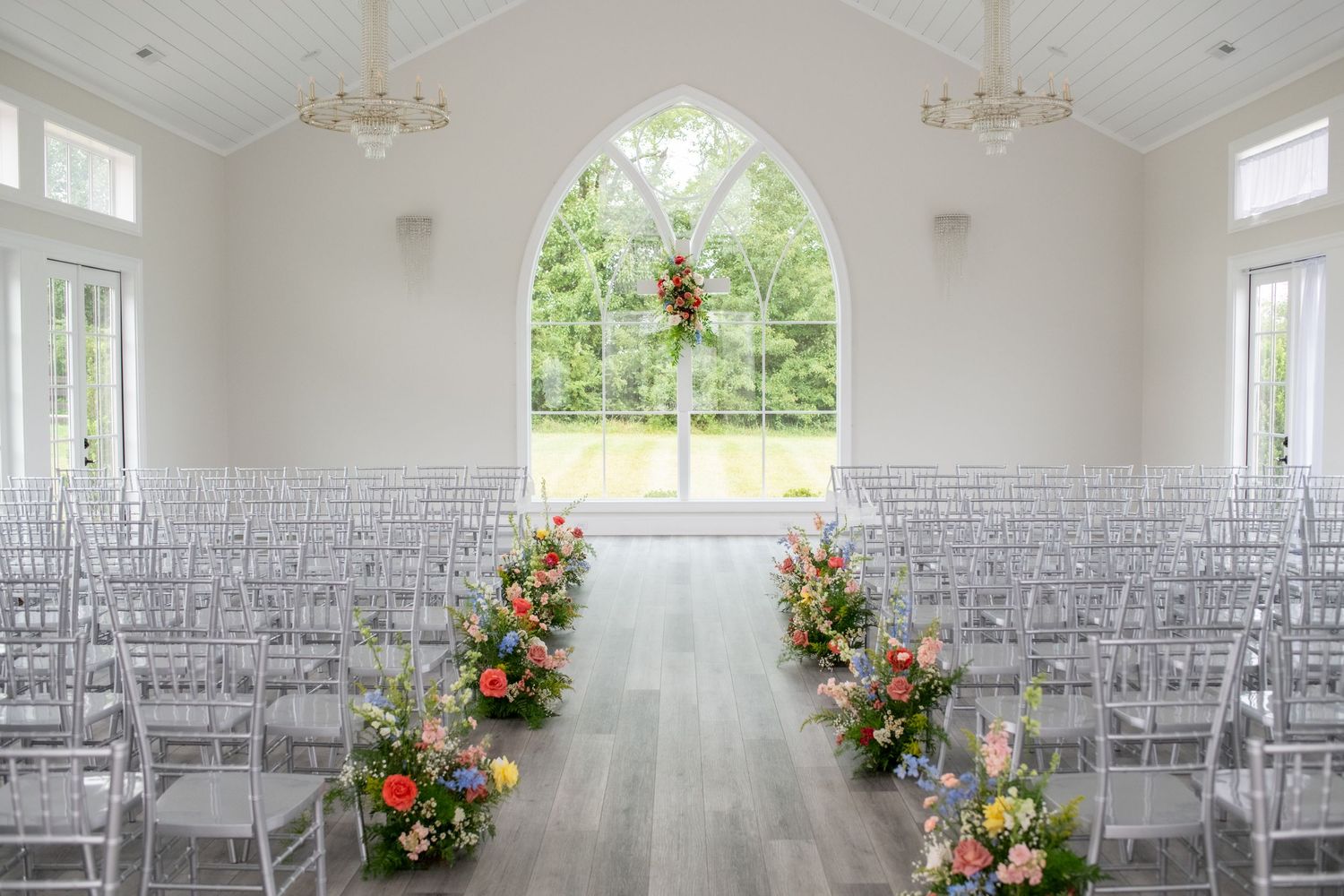 White wedding chapel interior with arched window and floral aisle decorations.