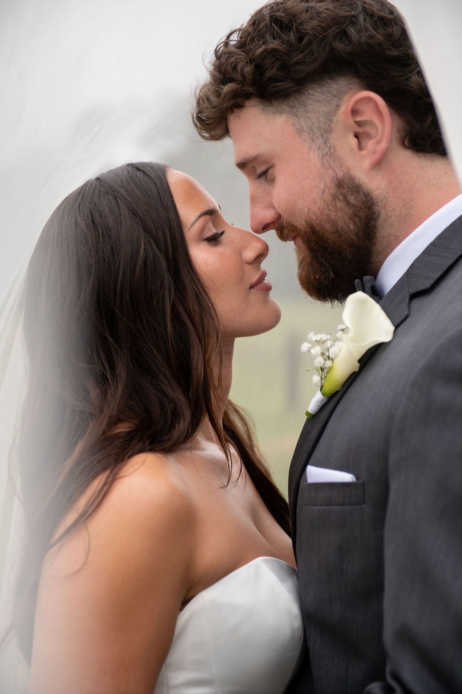 A bride and groom share a romantic almost-kiss moment, with the groom in a gray suit and boutonniere.