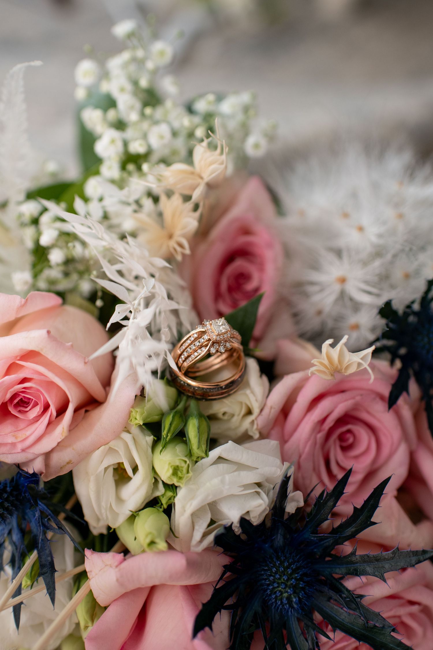 Pink roses and white flowers arranged with navy blue accents showcase wedding rings.