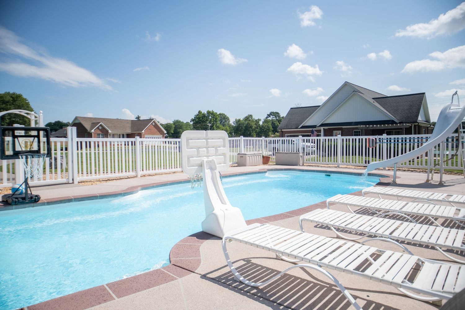 Large outdoor pool with curved edges surrounded by white railing and lounge chairs.