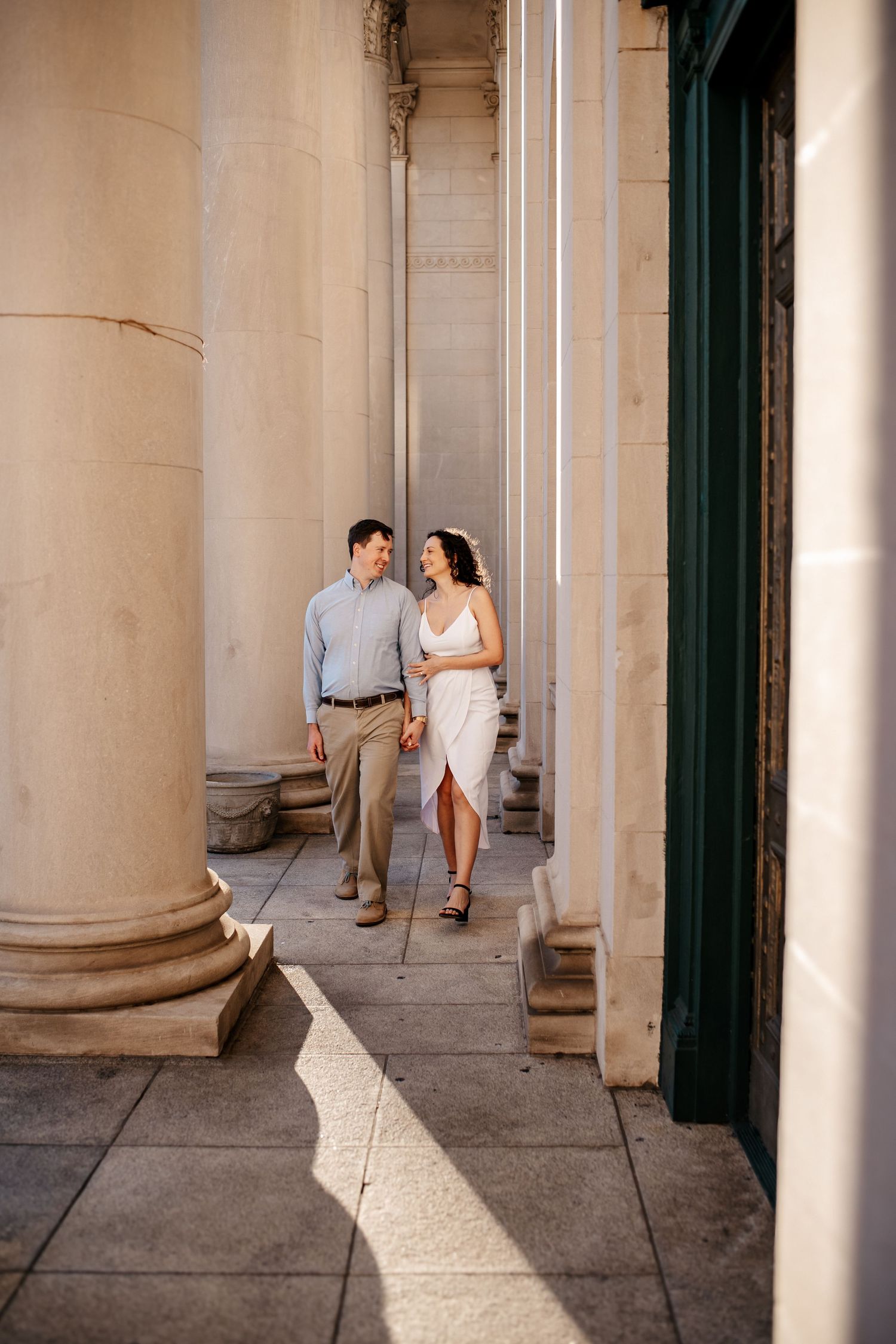 A couple walking between elegant classical columns in warm sunlight.