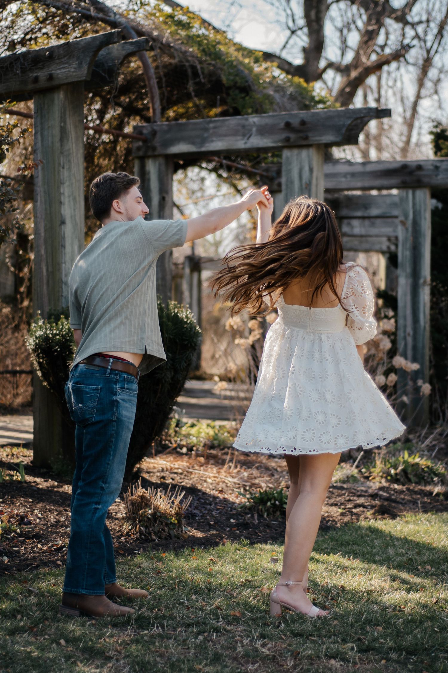 A playful couple dances and spins together in a garden setting during golden hour.