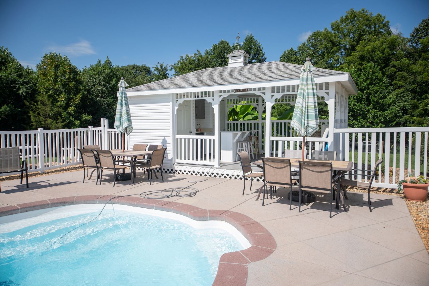 Resort-style swimming pool with white fencing and lounge chairs on a sunny day.