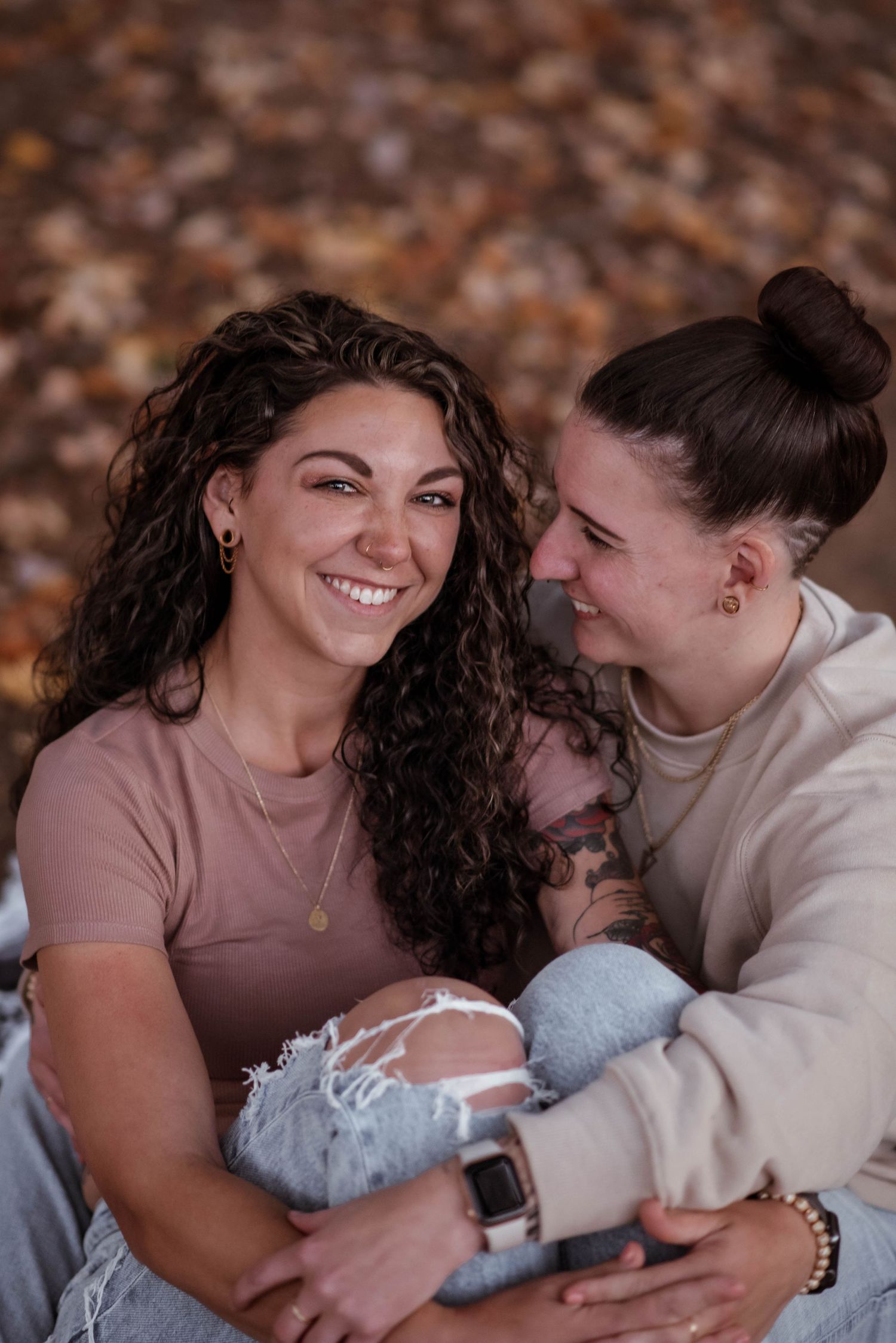 A couple shares an intimate moment while laughing and embracing on a fall day with blurred autumn foliage in the background.