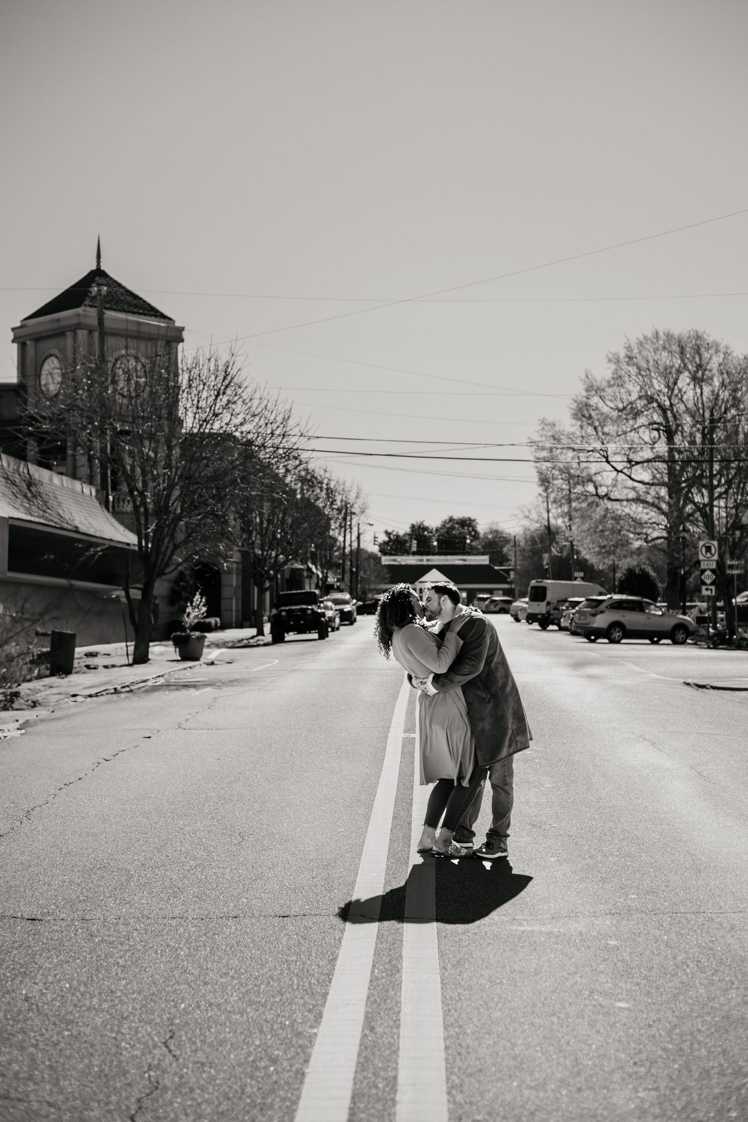 A romantic black and white photo on a small town street with a clock tower in the background.