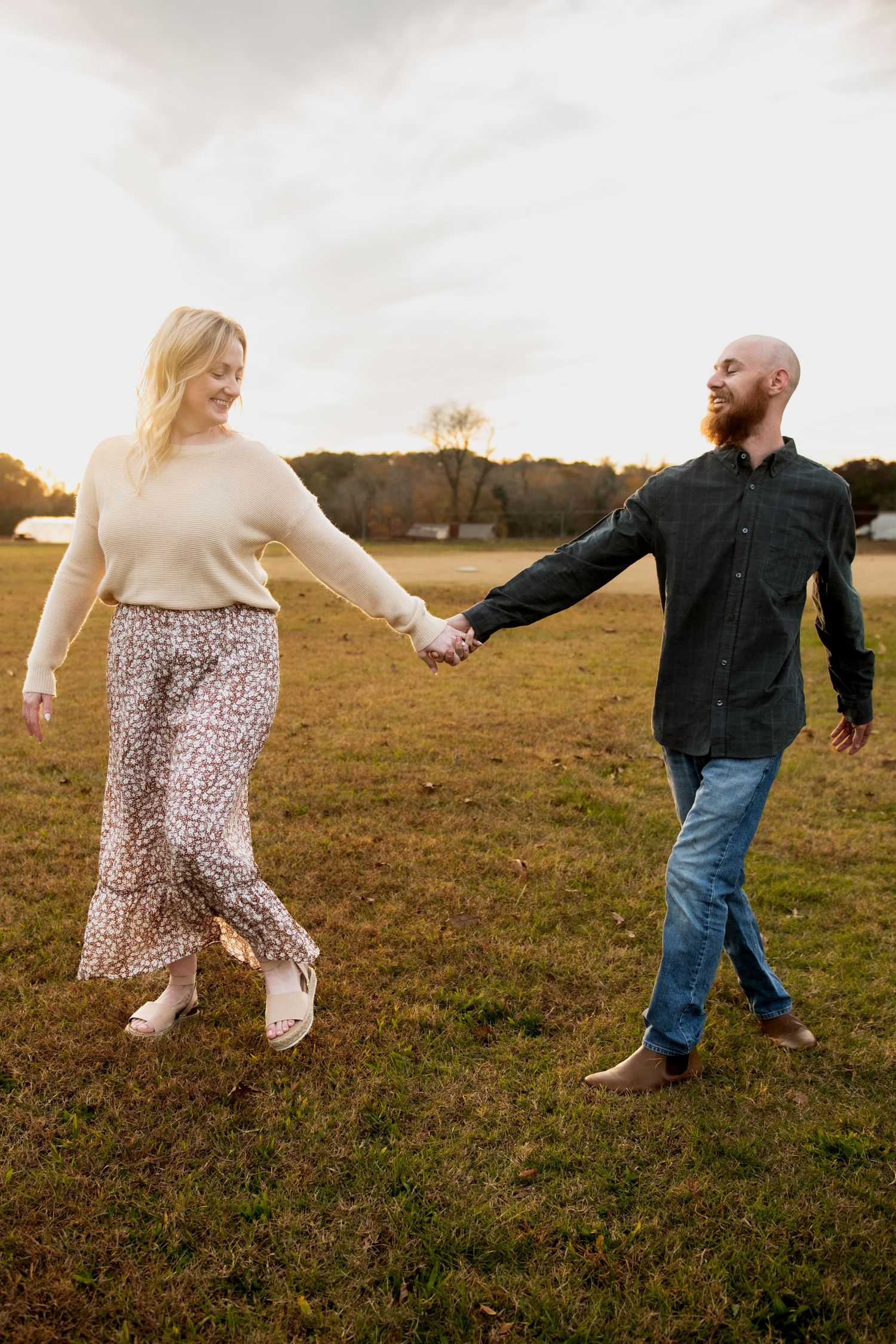 A couple playfully dances and spins together in a grassy field at golden hour.