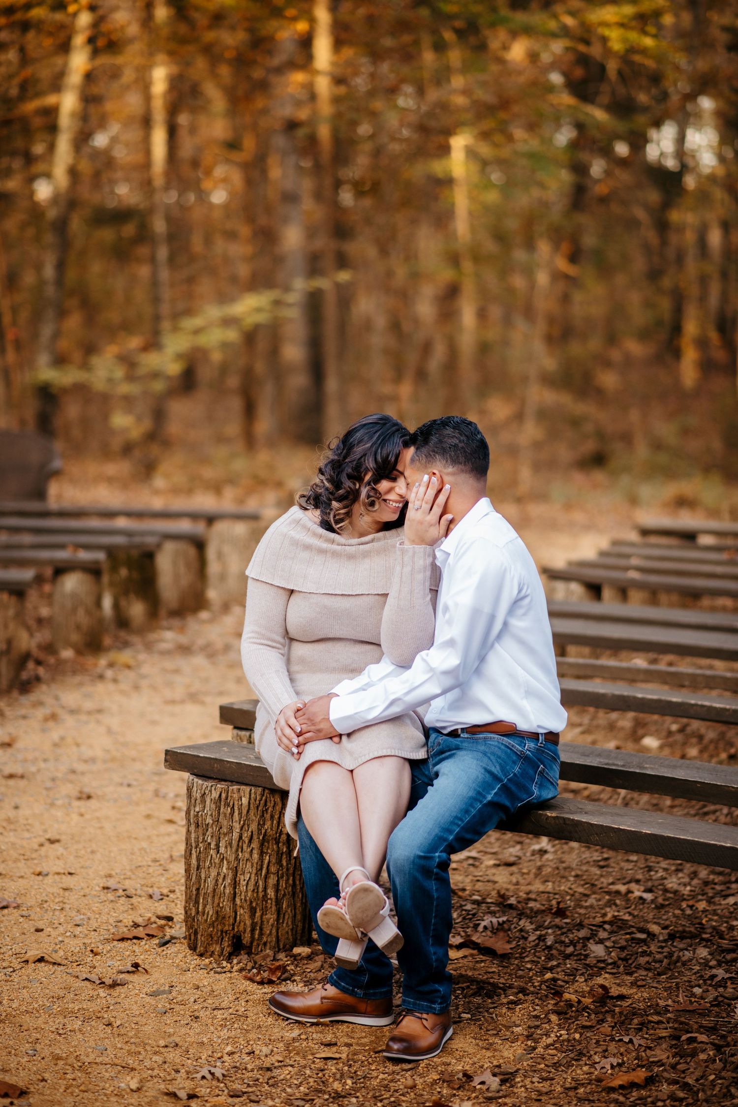 Couple sitting close together on wooden benches in an autumn forest setting.