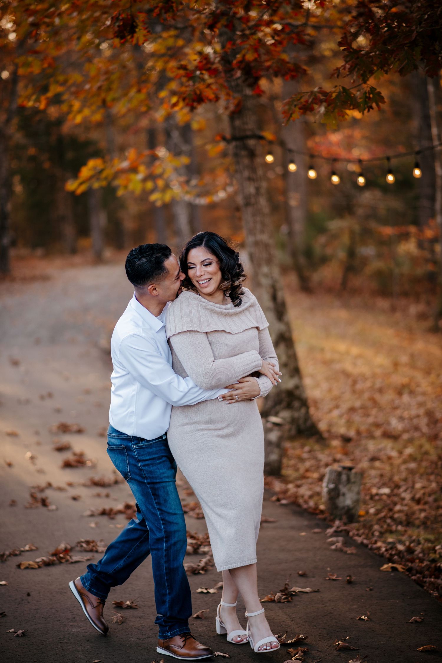 Couple sharing playful moments among fall leaves and string lights.
