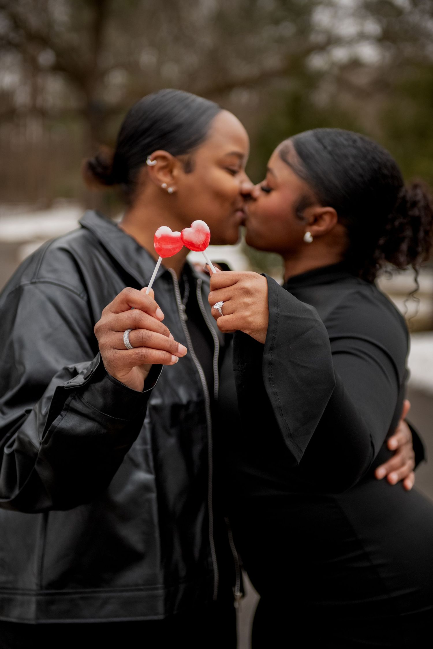 A tender moment shared between a couple holding heart-shaped lollipops outdoors.