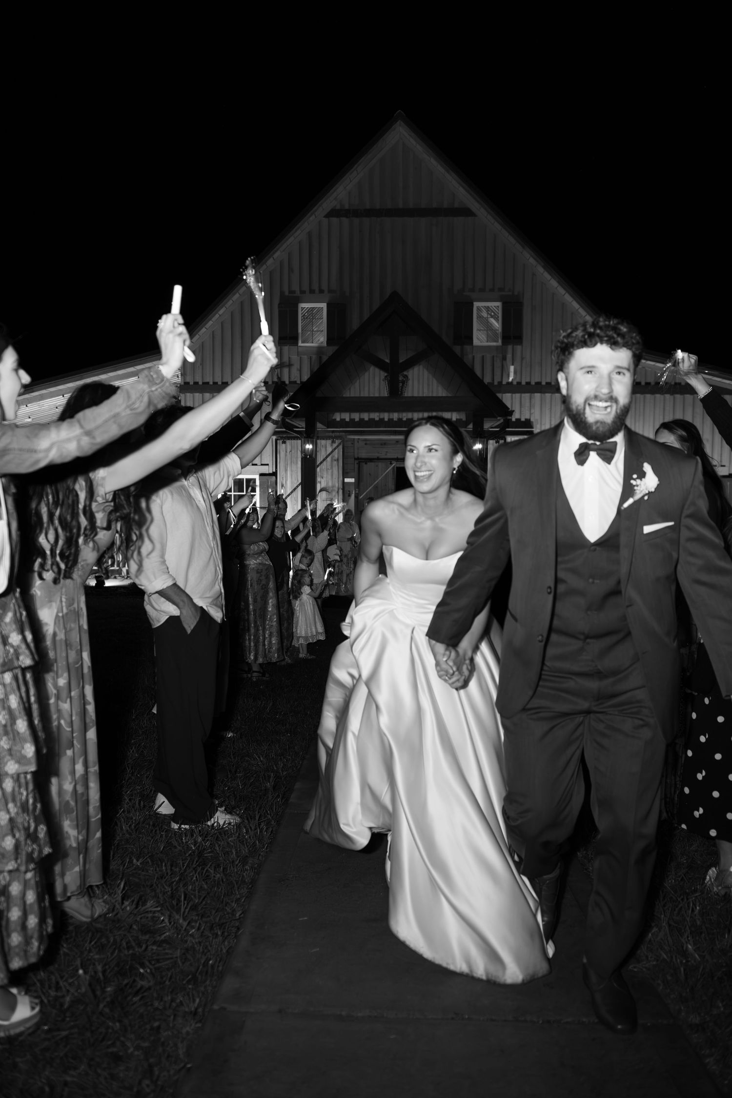 Black and white photo of a smiling bride and groom walking through a sparkler exit at their wedding reception.