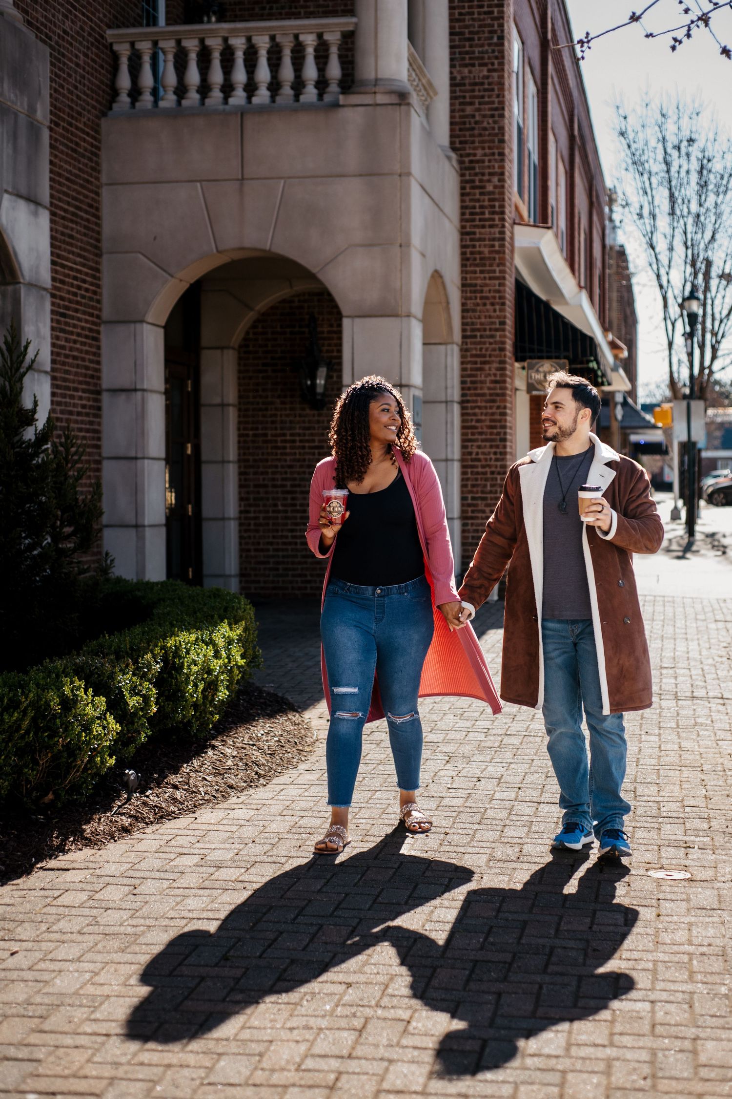 A couple walking along a brick building sidewalk on a sunny day.
