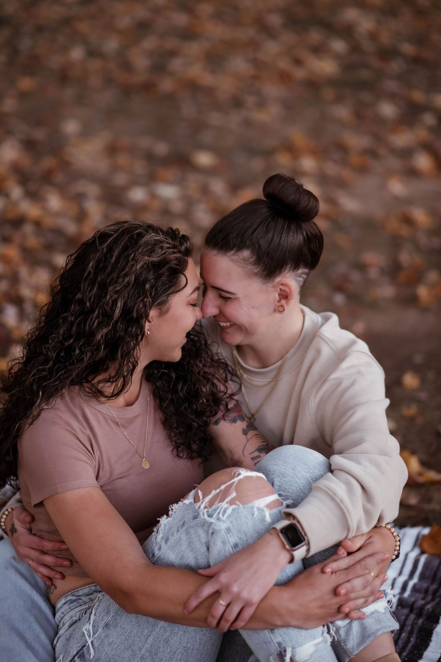 A couple shares tender moments while sitting together on fallen autumn leaves in a romantic outdoor setting.