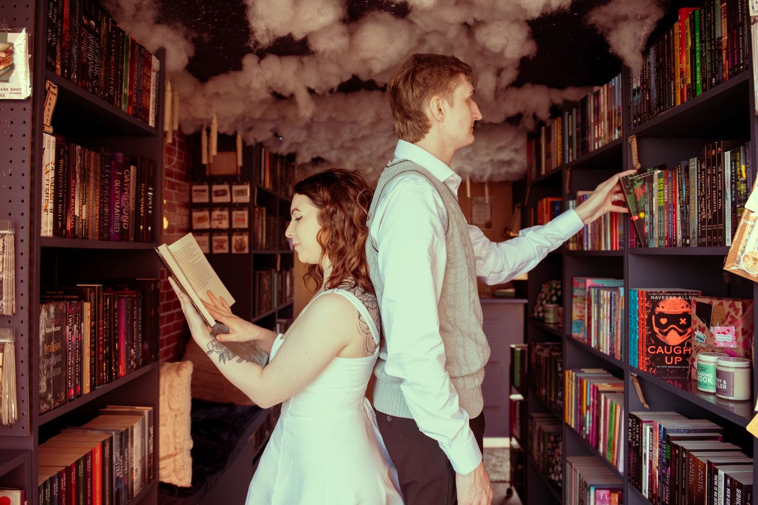 A couple reads books in a whimsical library with dark clouds swirling among colorful shelves.