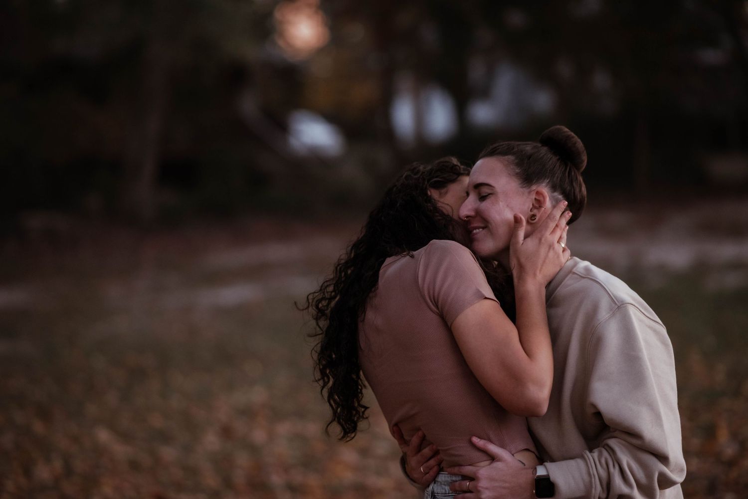 A romantic couple embraces in a moody outdoor setting with autumn leaves and natural lighting.