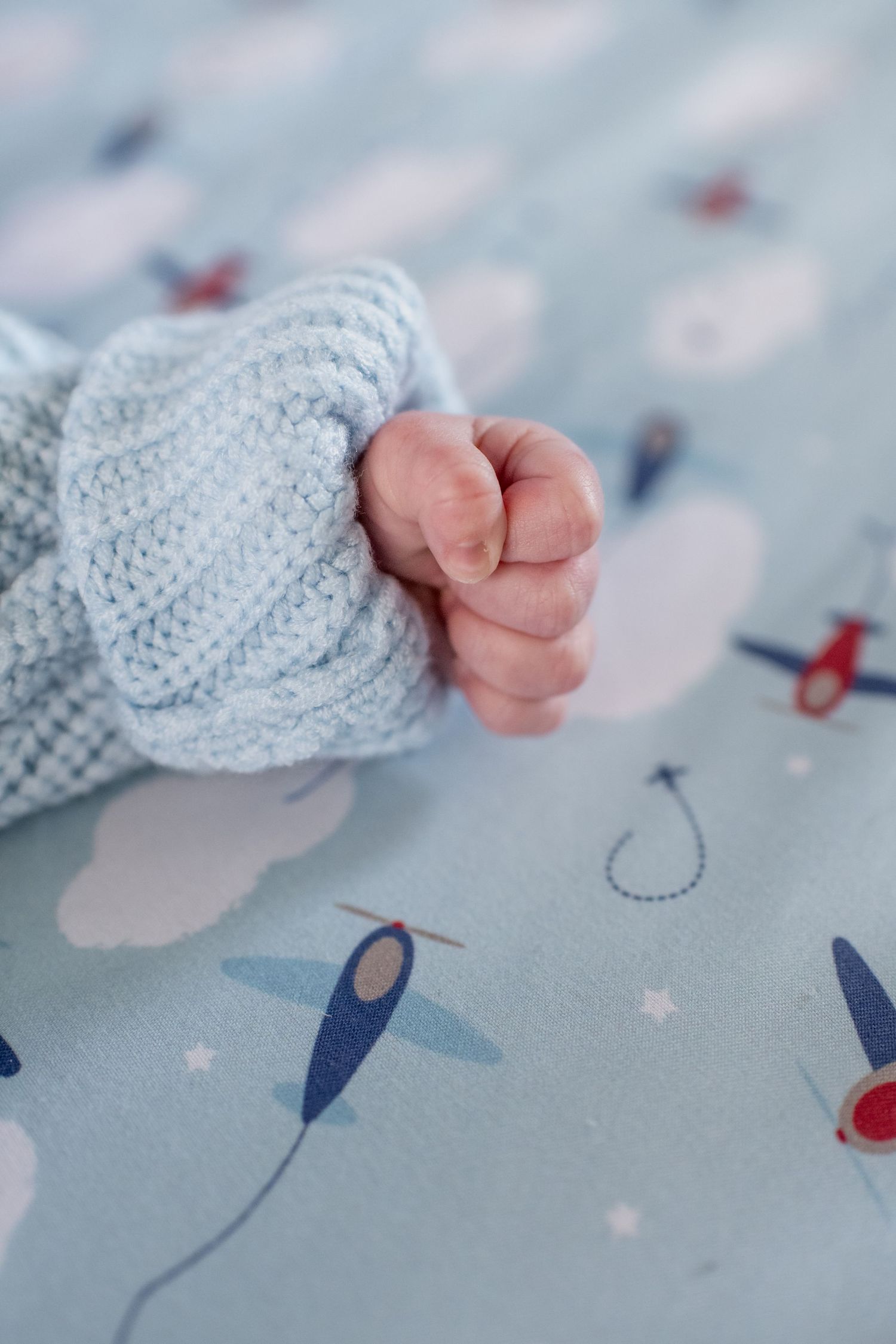 Close-up of tiny baby toes peeking out from a knitted gray sweater on airplane-patterned fabric.