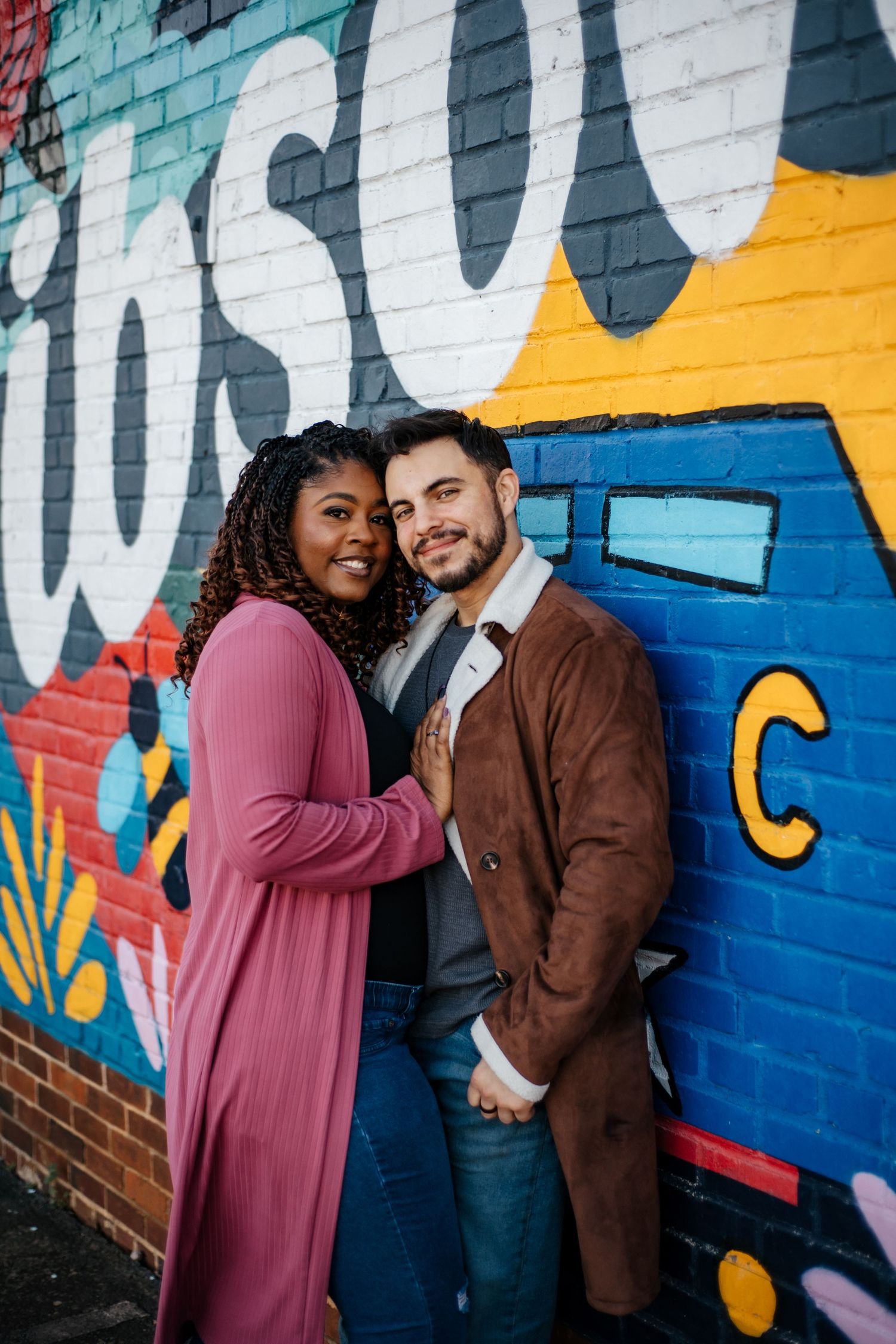 Couple posing playfully against a vibrant graffiti wall with blue and yellow artwork.